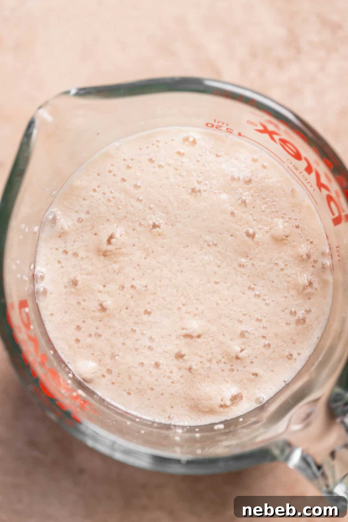 A glass measuring cup with foamy and active yeast, indicating it's ready for use in baking.