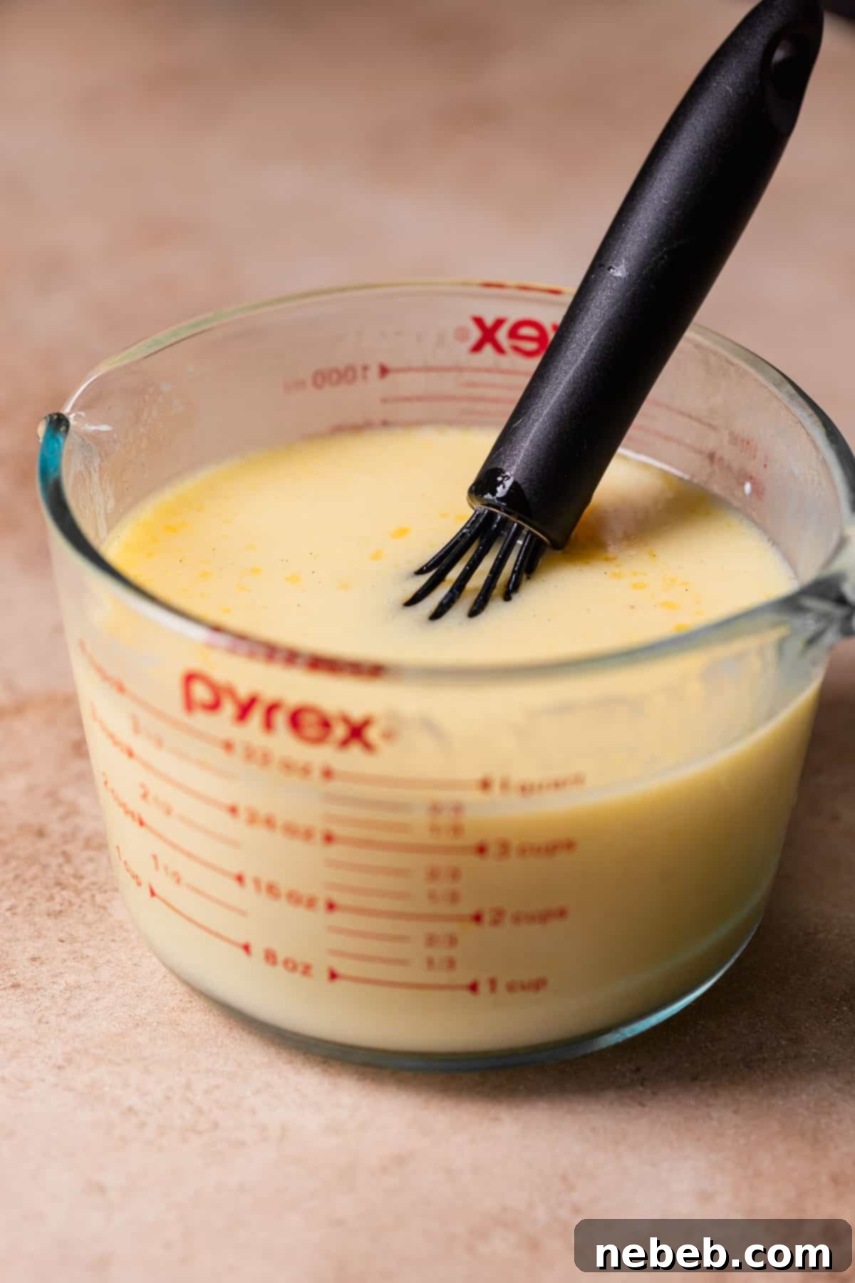 A glass bowl with the whisked wet ingredients for the muffin batter, including buttermilk, eggs, and melted butter.