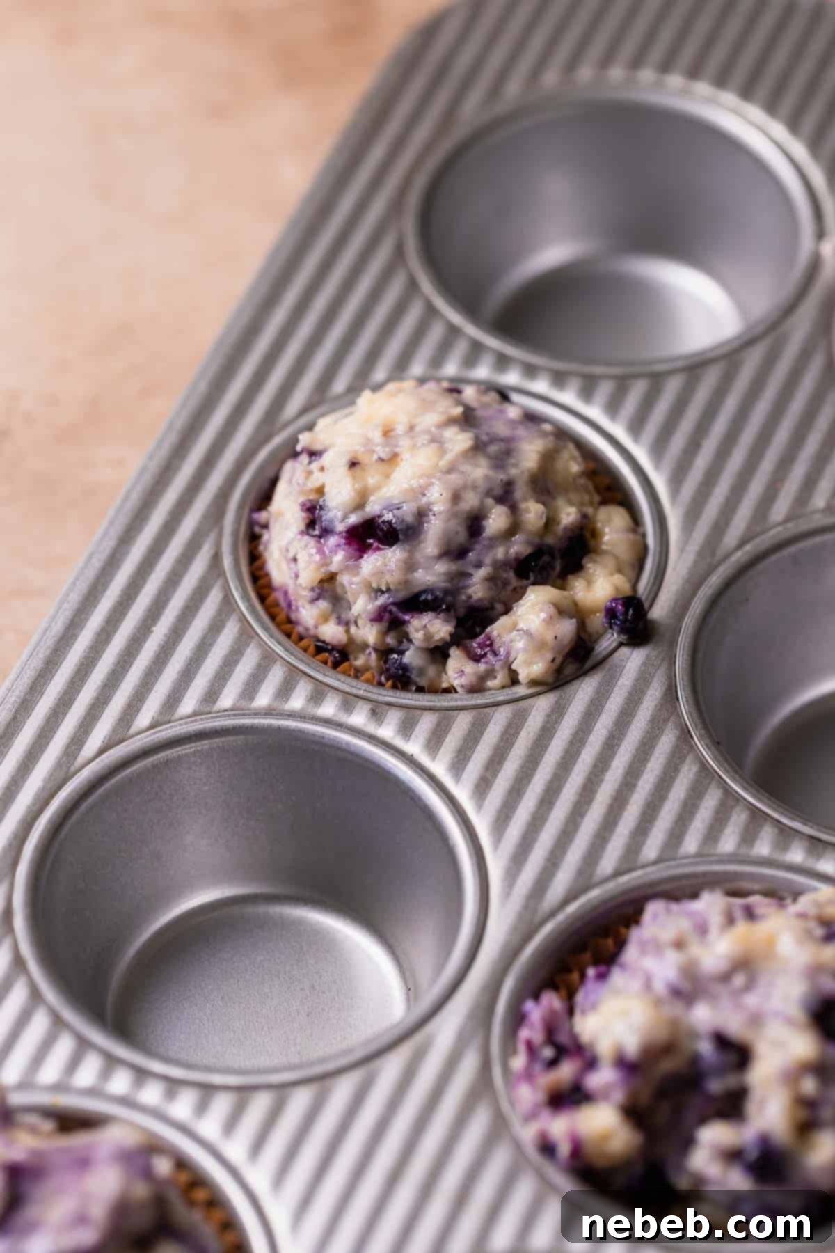 A muffin pan lined with paper liners and generously filled with blueberry muffin batter, ready for baking.