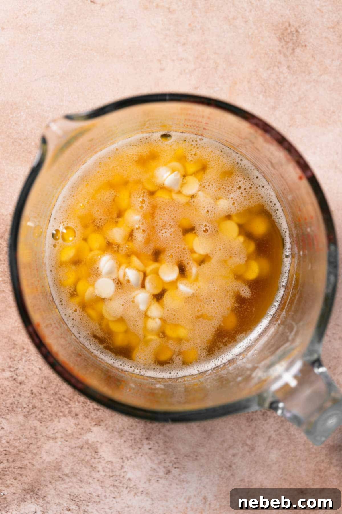 A bowl with warm browned butter and white chocolate chips, melting together to form a smooth mixture.