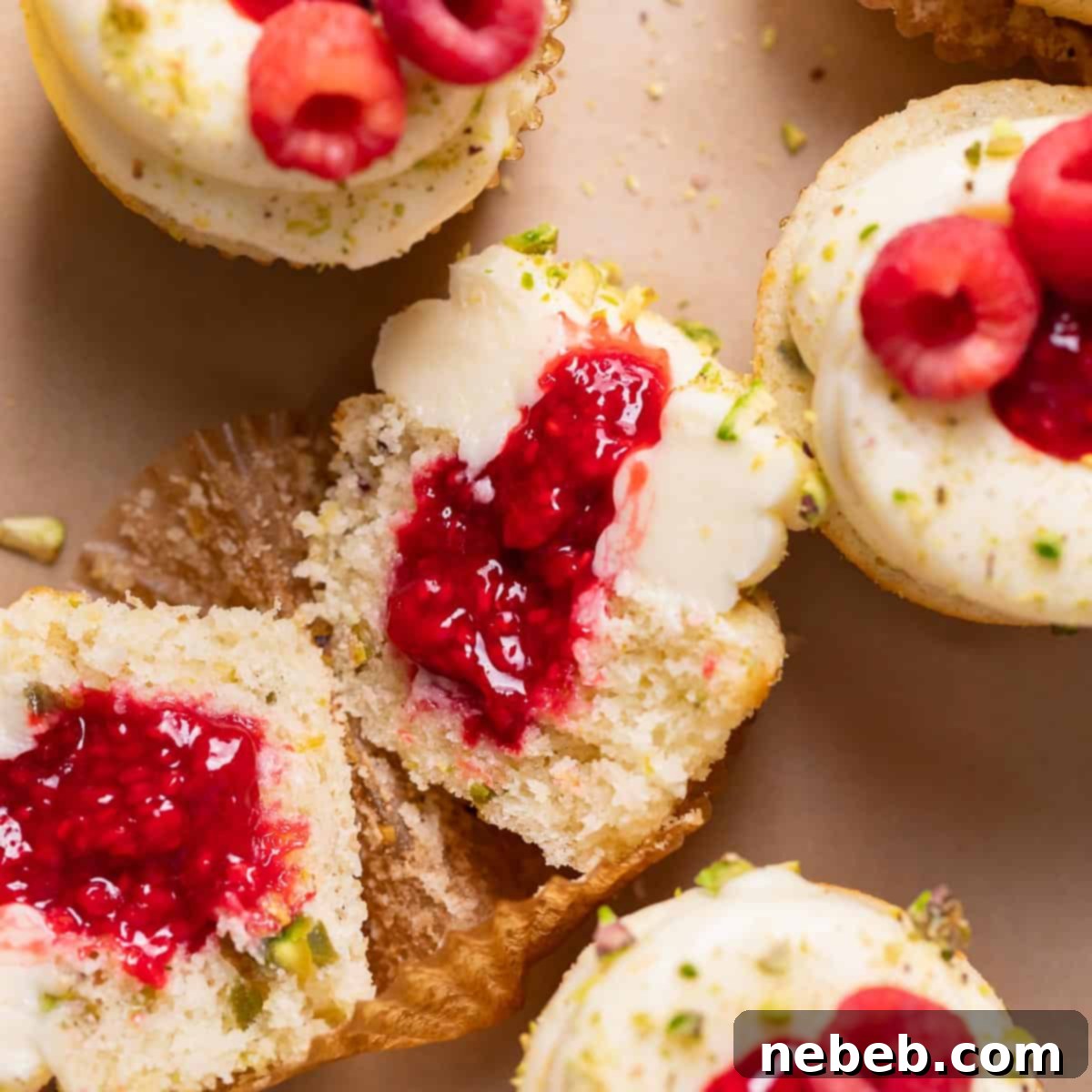 Moist lemon cupcakes with vibrant raspberry filling cut in half, showcasing the layered flavors and beautiful presentation. Garnished with fresh raspberries and a hint of pistachio, ready to impress at any spring or summer gathering.