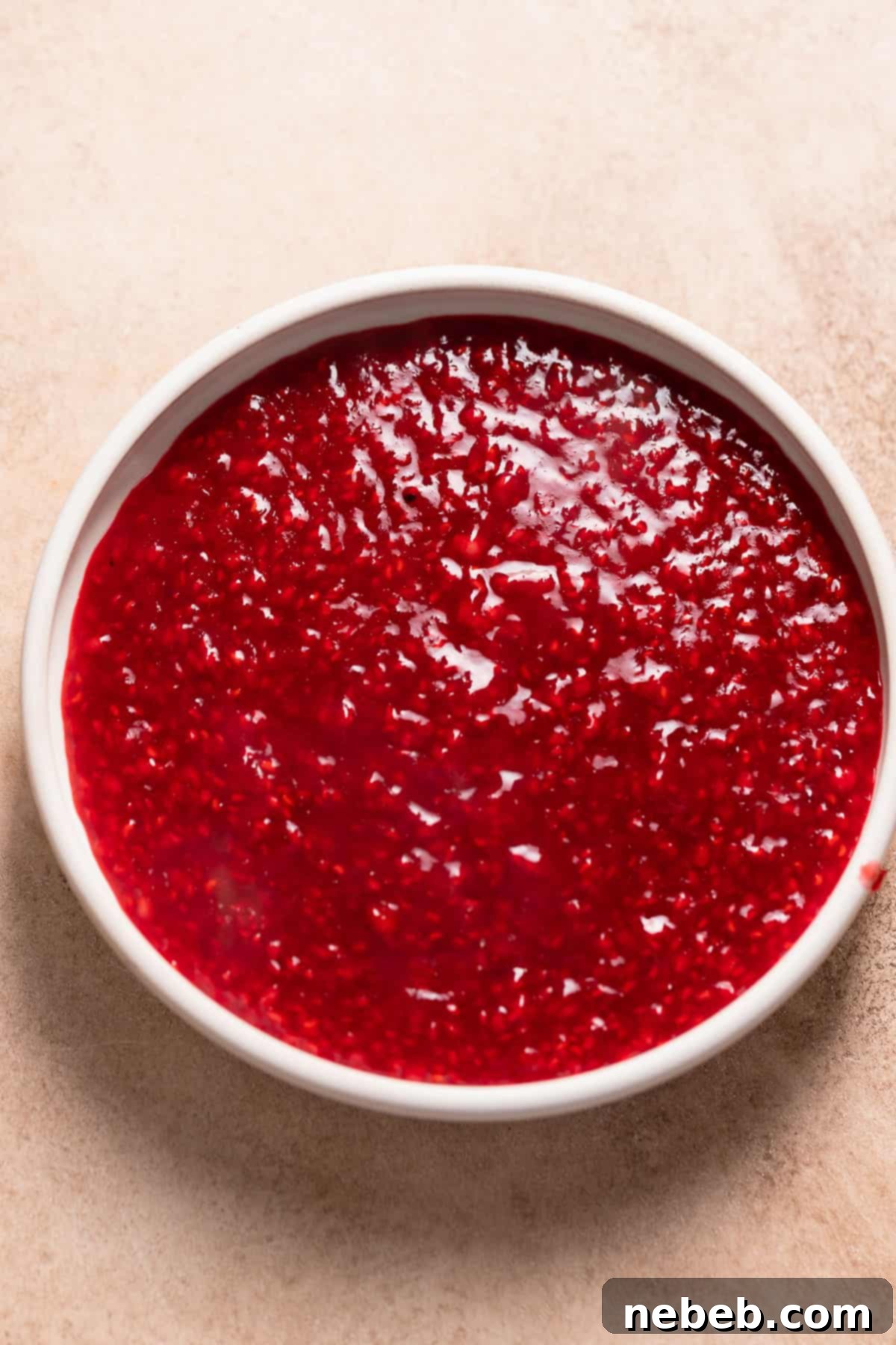 Vibrant red homemade raspberry jam in a white bowl, ready to be used as filling for cupcakes.