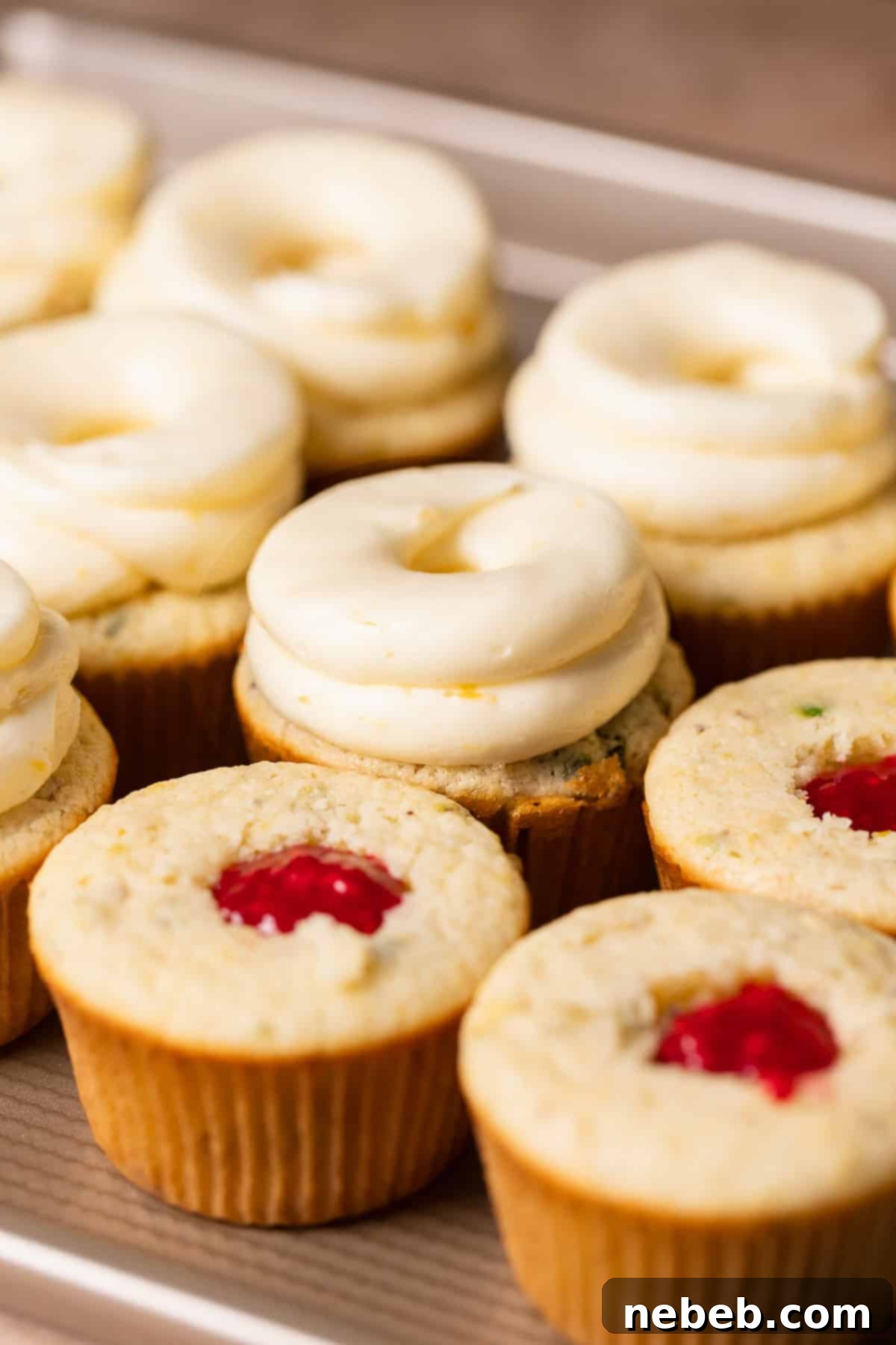 Half-frosted lemon raspberry cupcakes on a baking tray, with some centers filled with jam and buttercream piped around the edges.