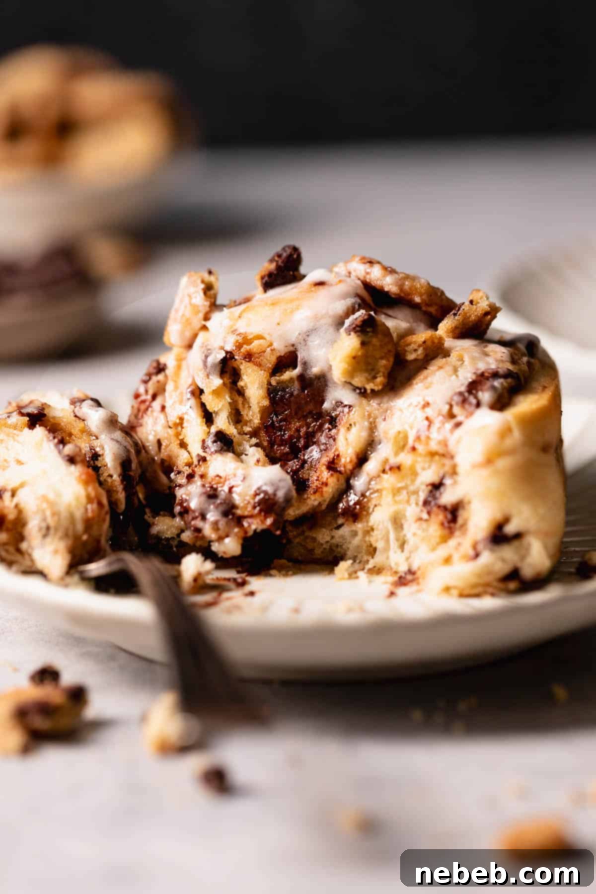 A cinnamon roll stuffed with cookie dough on a plate being eaten.