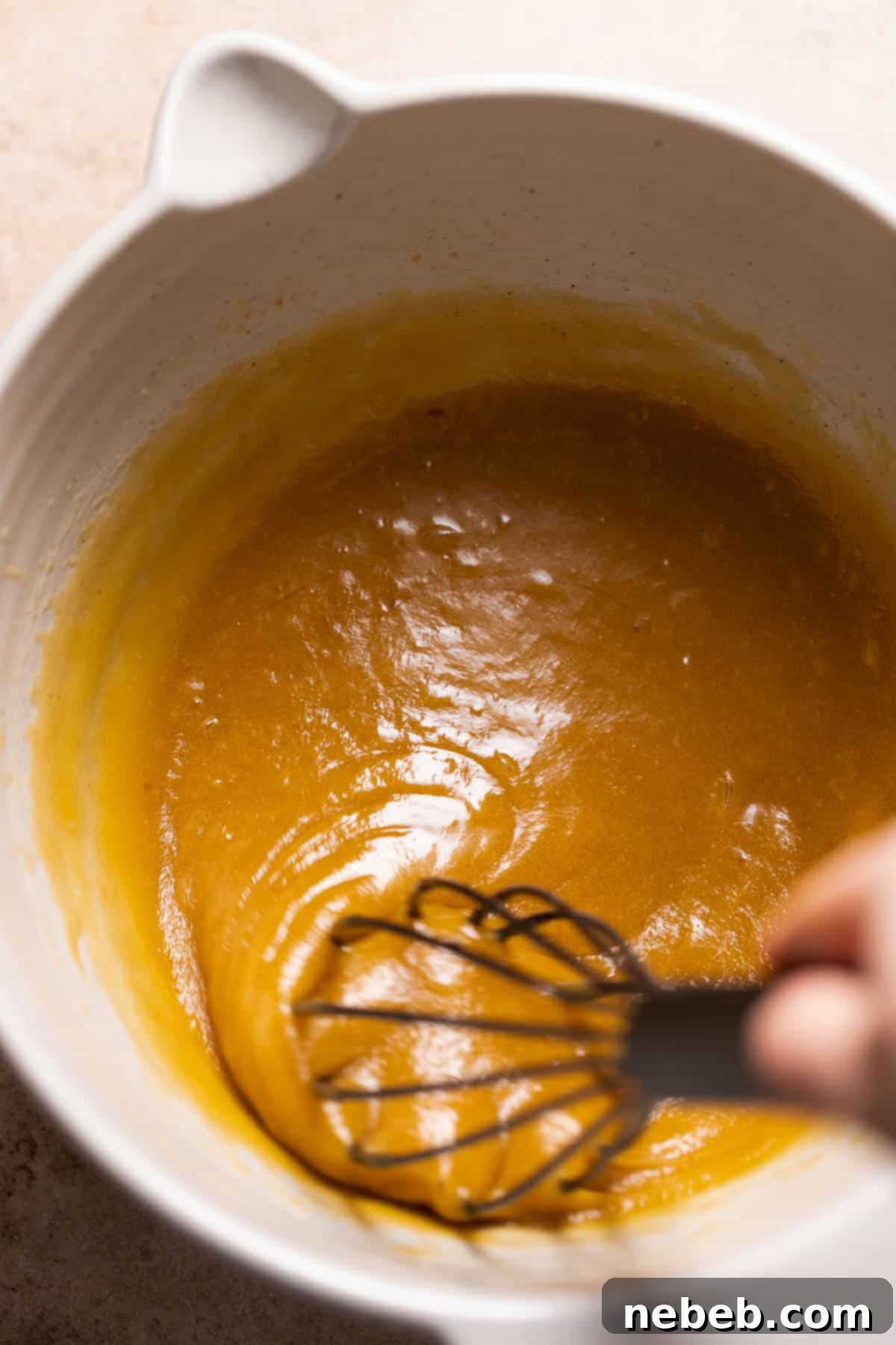 A whisk mixing the eggs and vanilla into the butter and sugar.