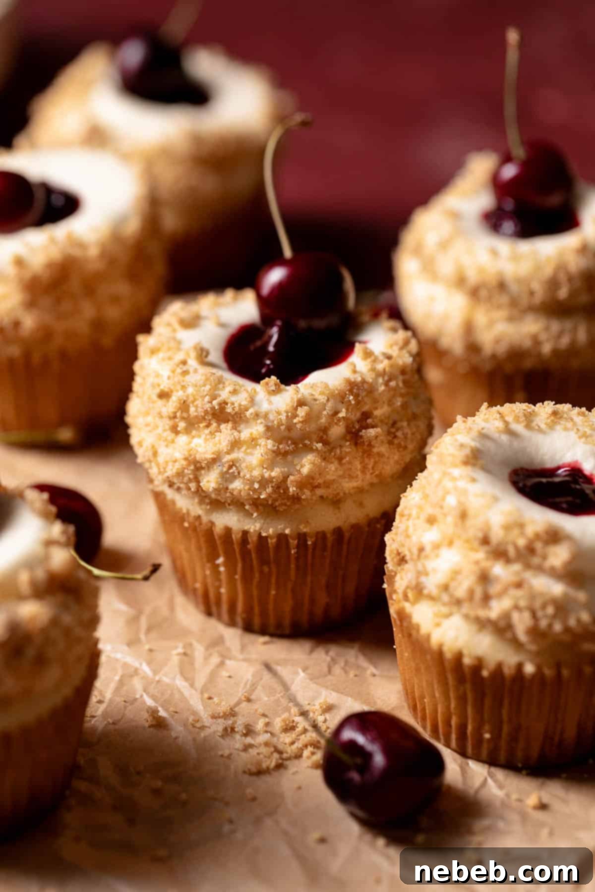 Close-up of a cherry cheesecake cupcake with cherry filling, graham cracker crumbs, and cream cheese frosting, ready to be enjoyed.