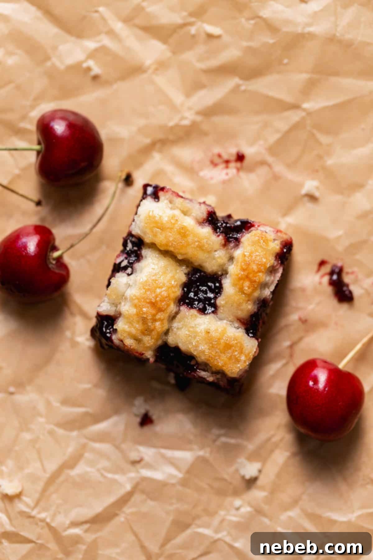A delicious homemade cherry pie bar with golden-brown pie crust on brown parchment paper, artfully arranged with fresh red cherries beside it.