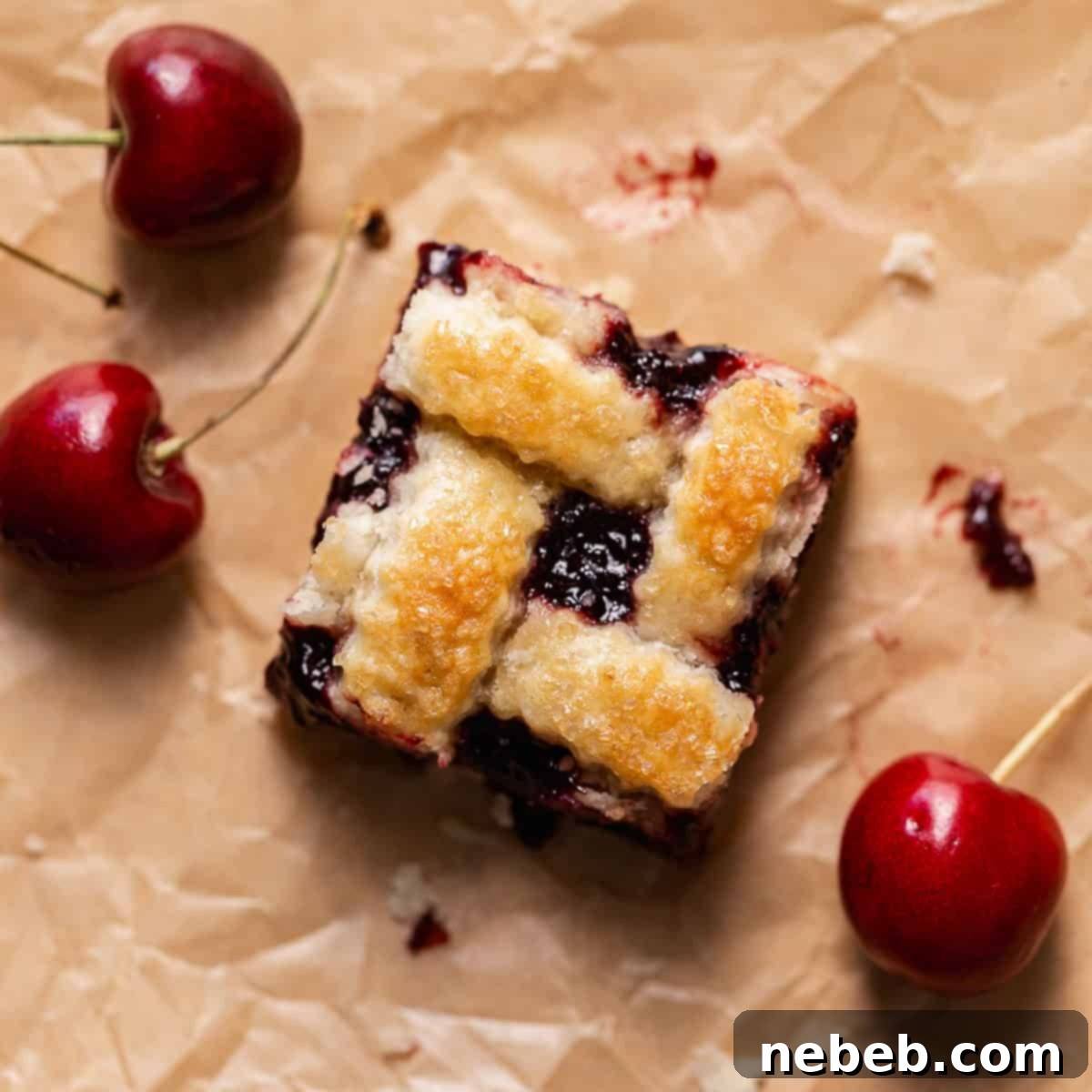 A perfectly baked cherry pie bar on brown parchment paper, invitingly surrounded by a scattering of fresh, vibrant red cherries.