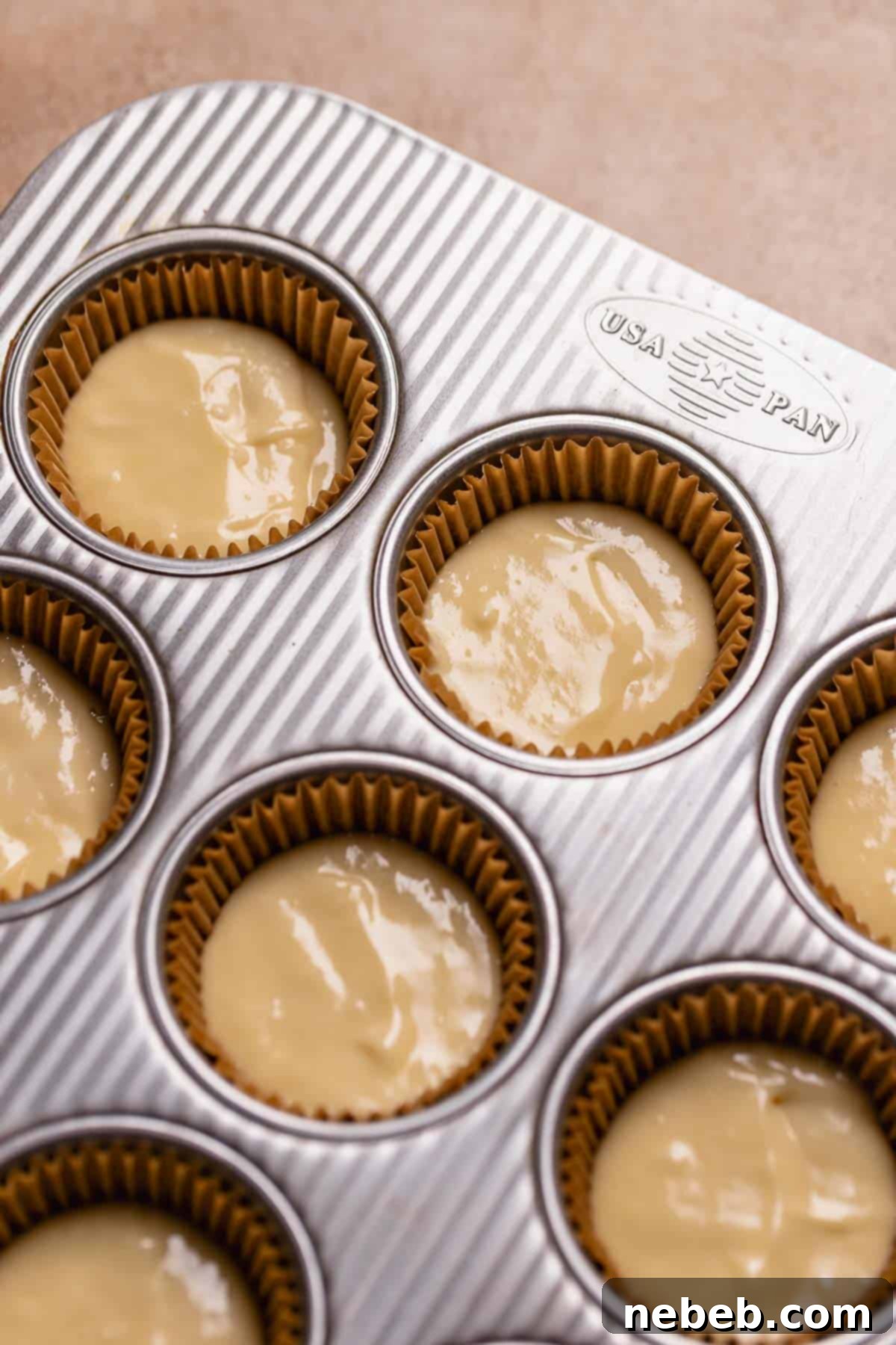 A cupcake pan with liners half full of cupcake batter before baking, perfectly portioned.