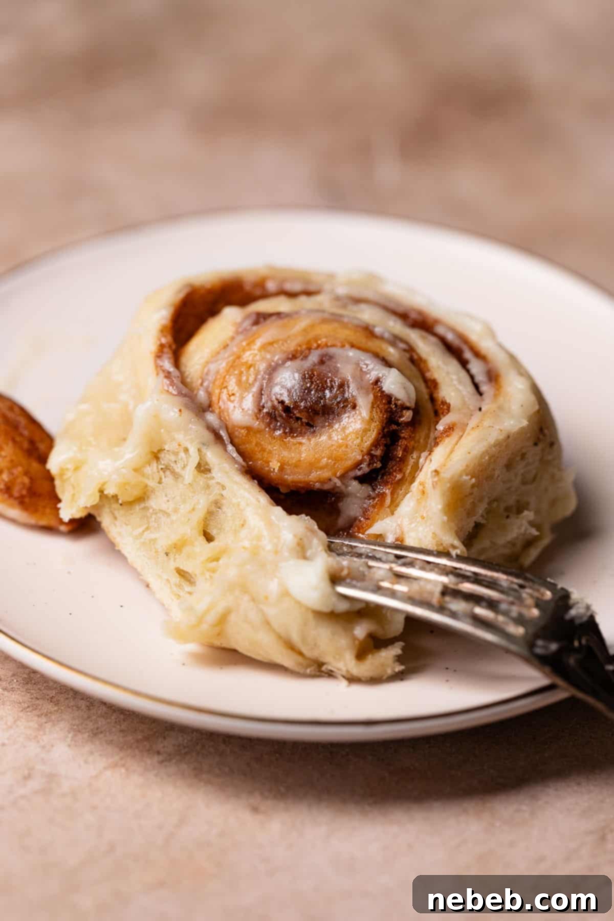 Brown butter cinnamon roll on a white plate with a fork digging into it.