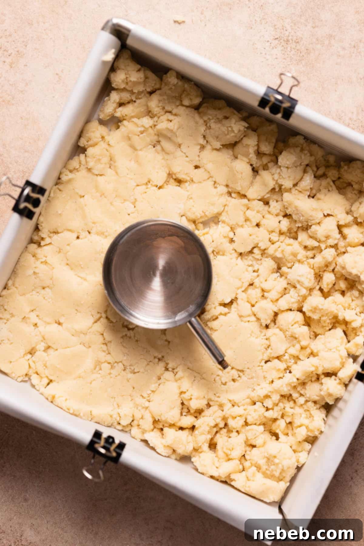 Shortbread crumbs being pressed evenly into a baking pan, ready for baking.