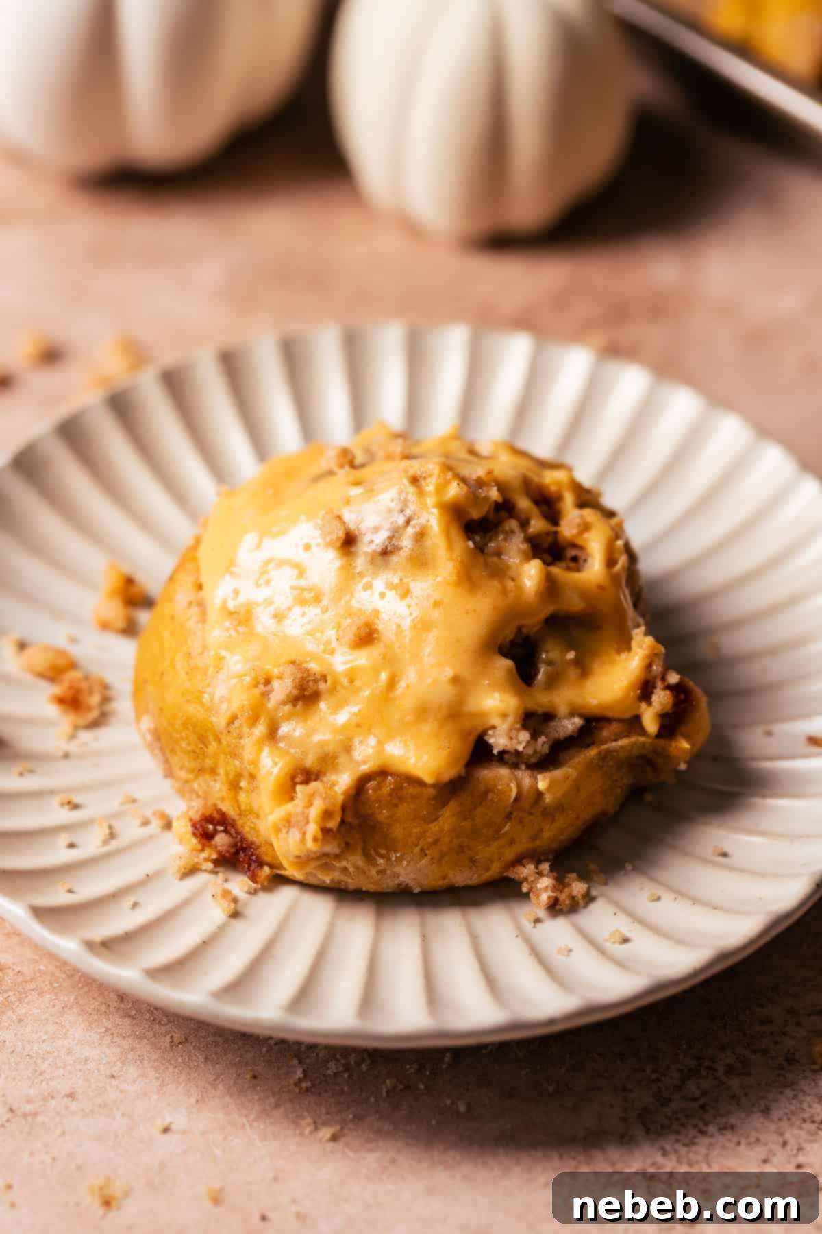 A single, perfectly frosted pumpkin cinnamon roll placed delicately on a white plate, ready to be eaten.