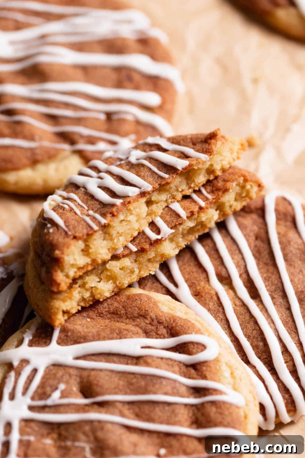 A delicious cinnamon bun cookie broken in half to clearly show its luscious cinnamon sugar layer nestled within the soft cookie and topped with creamy frosting.