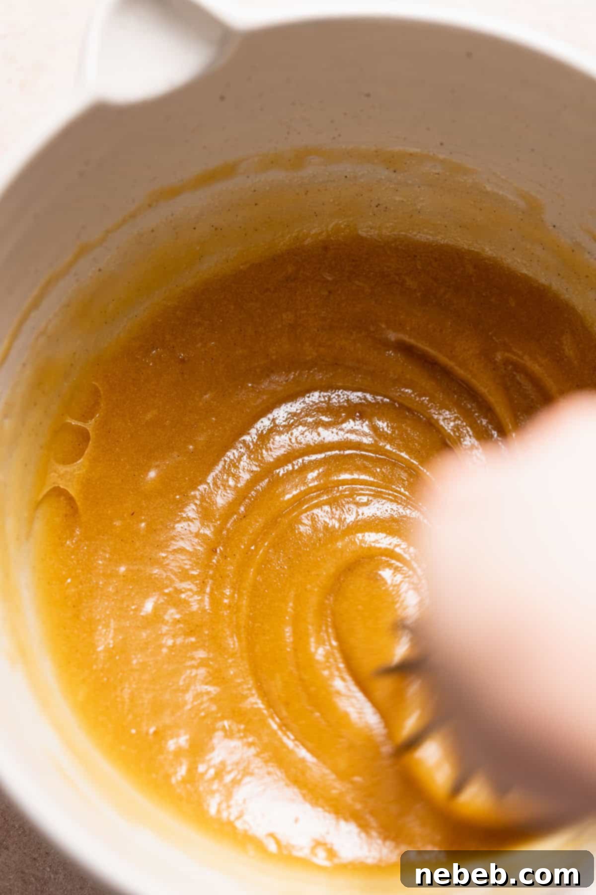 A whisk vigorously mixing the eggs into the butter and sugar mixture, creating a glossy and thickened texture.