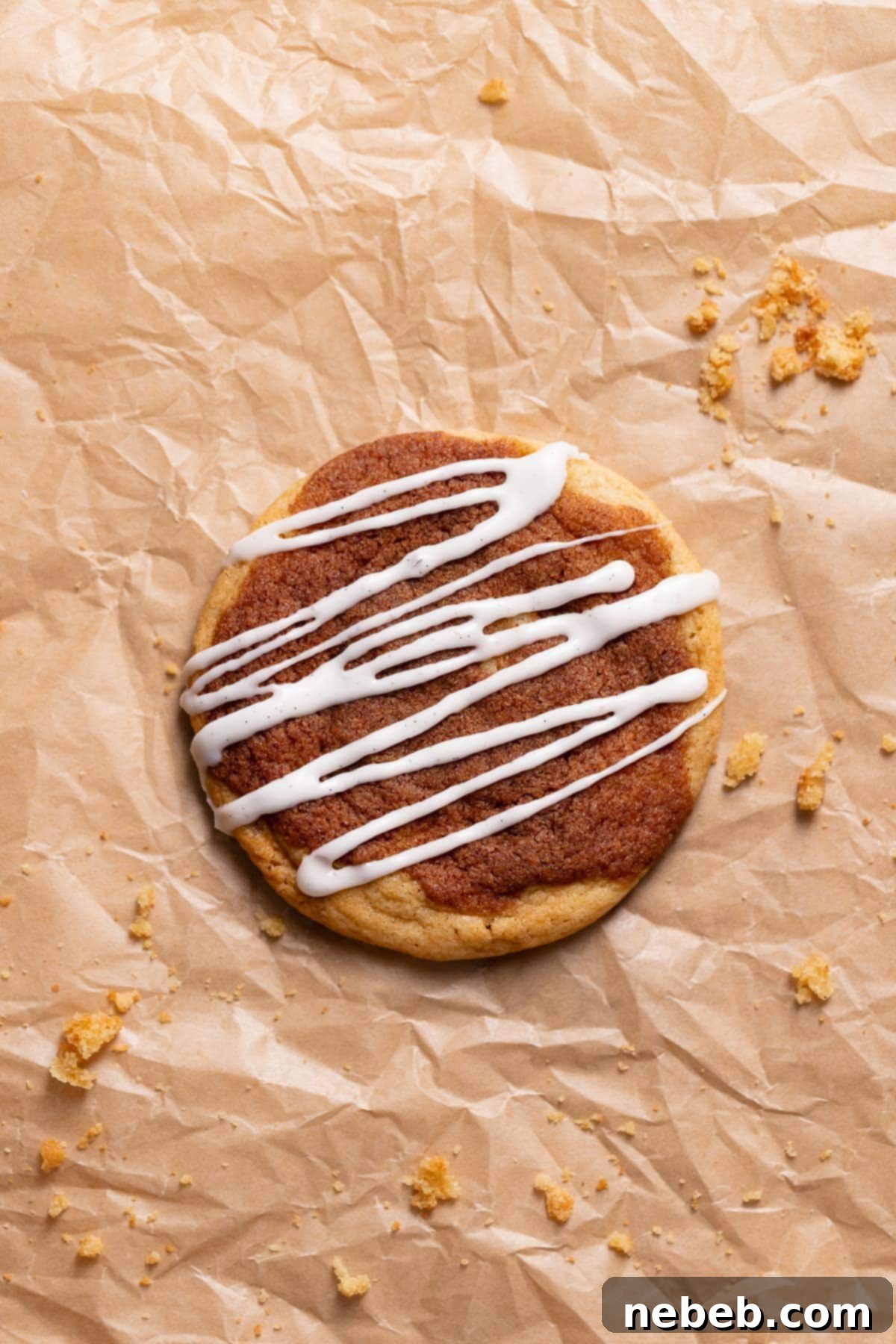A freshly baked cinnamon roll cookie resting on parchment paper, beautifully drizzled with luscious cream cheese icing, ready to be enjoyed.