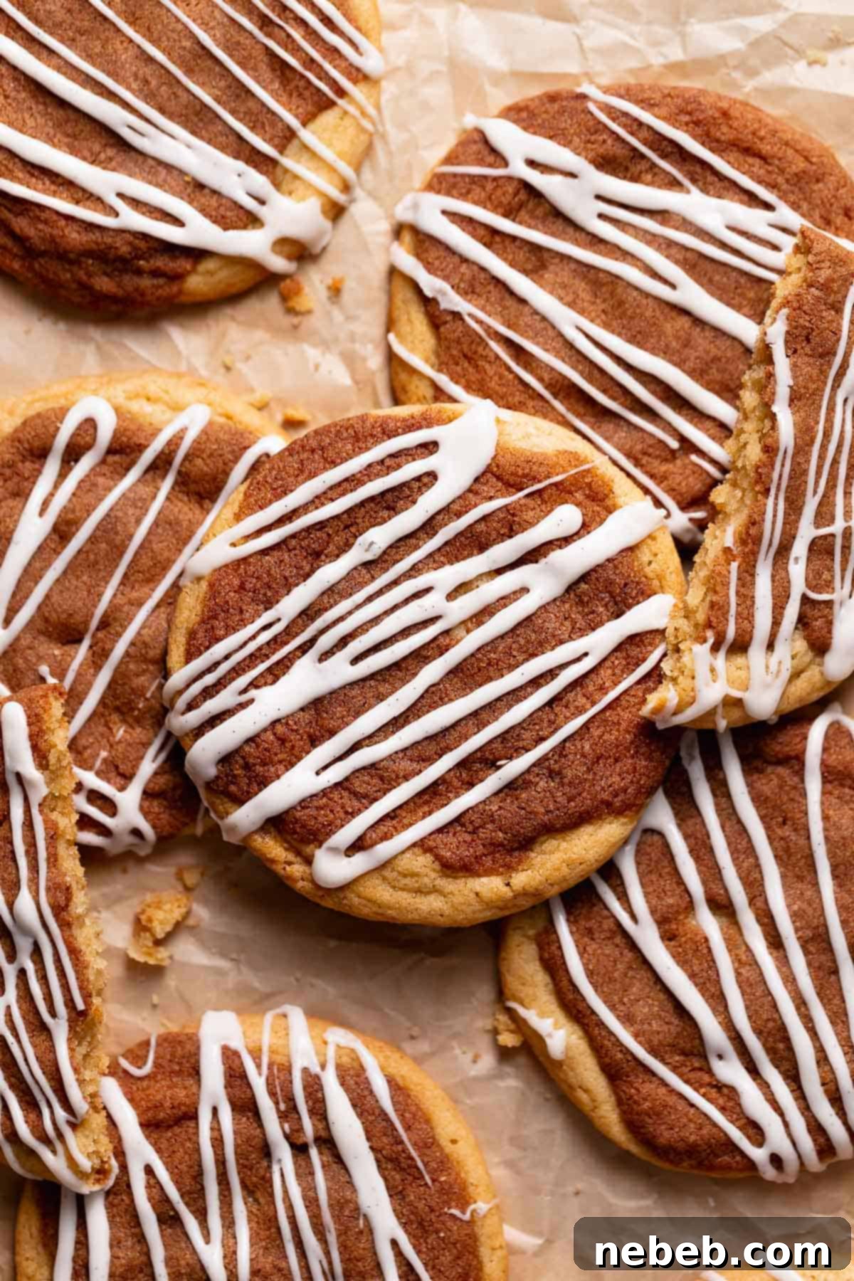 A close-up shot of multiple cinnamon roll cookies, showing their textured cinnamon sugar tops and generous drizzles of vanilla cream cheese icing on a white plate.