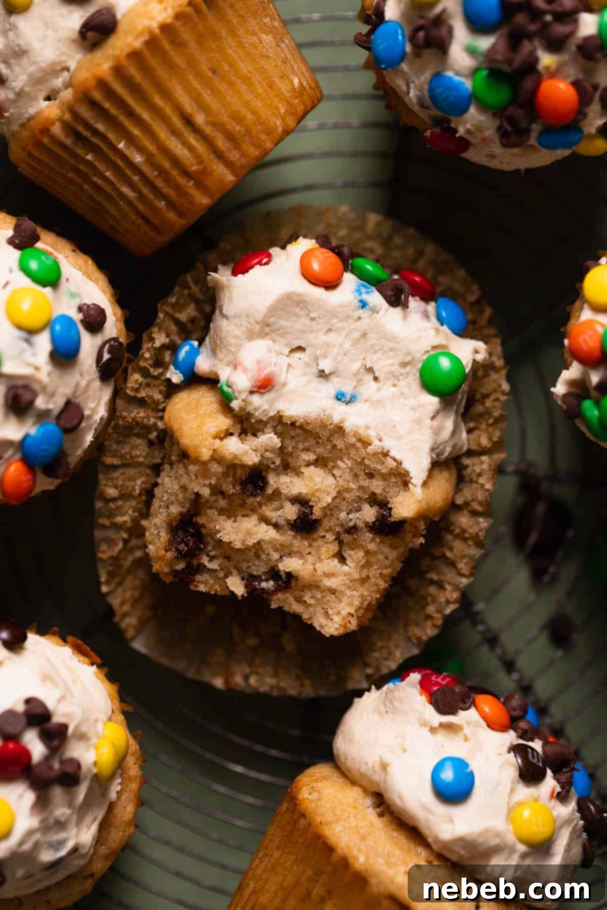 Monster cookie cupcakes on a wire cooling rack with a bite taken out of one, showcasing the M&Ms and chocolate chips within.
