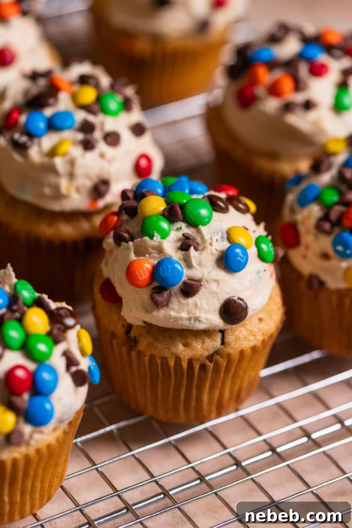 Monster cookie cupcakes on a wire rack after decorating, showing the frosted tops and toppings.