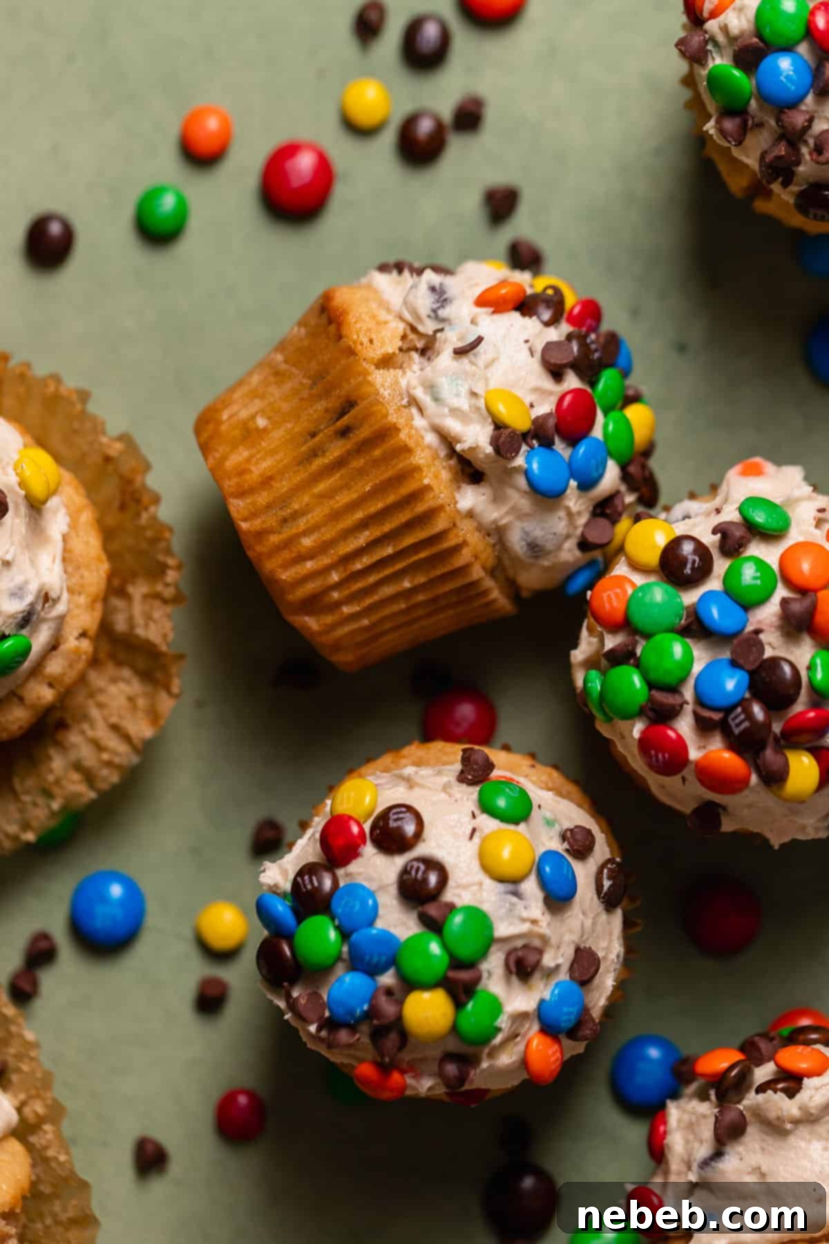 Monster cookie dough cupcakes on a vibrant green backdrop, highlighting their colorful toppings and appealing texture.