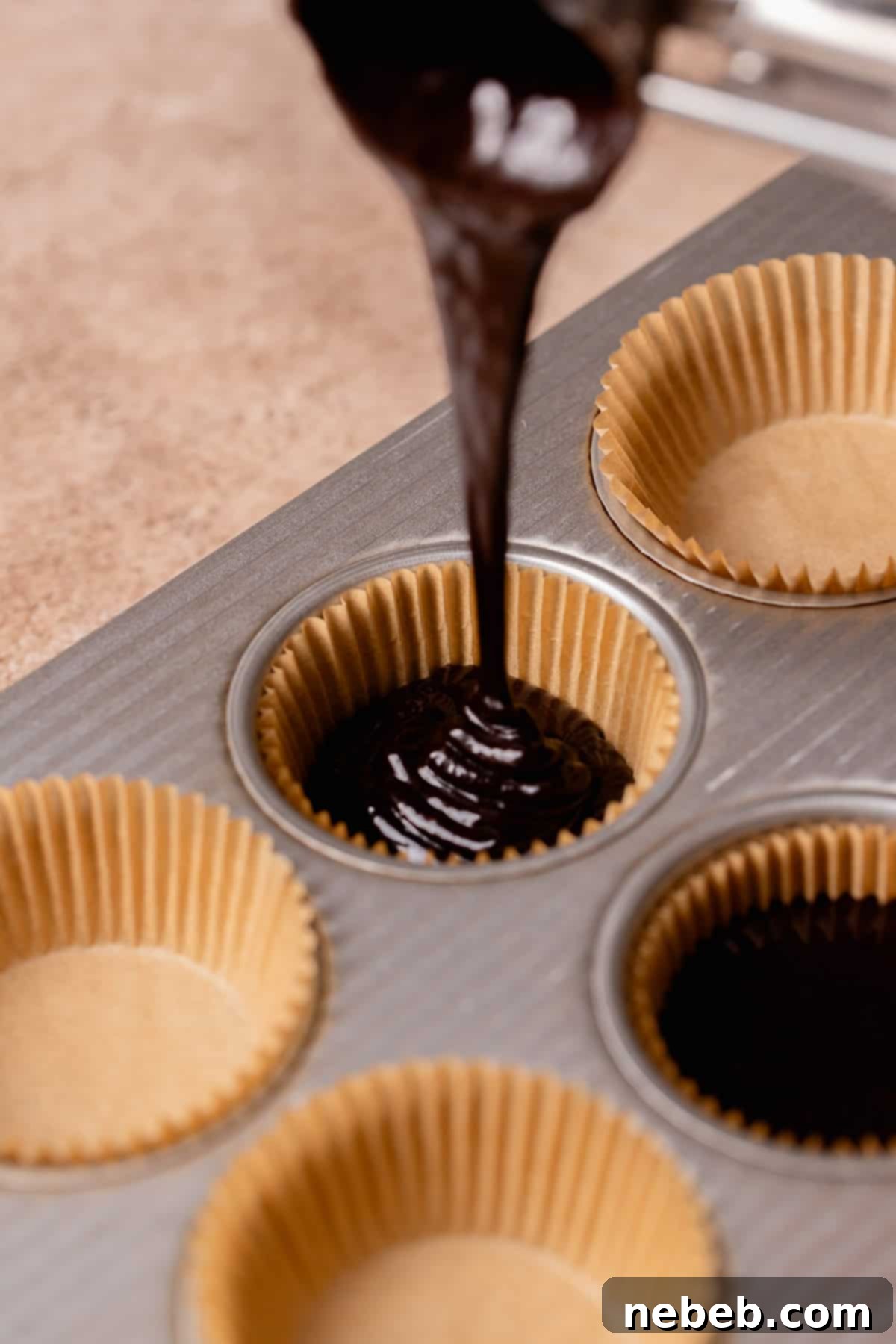 Black cupcake batter being poured into cupcake liners in a muffin tin.