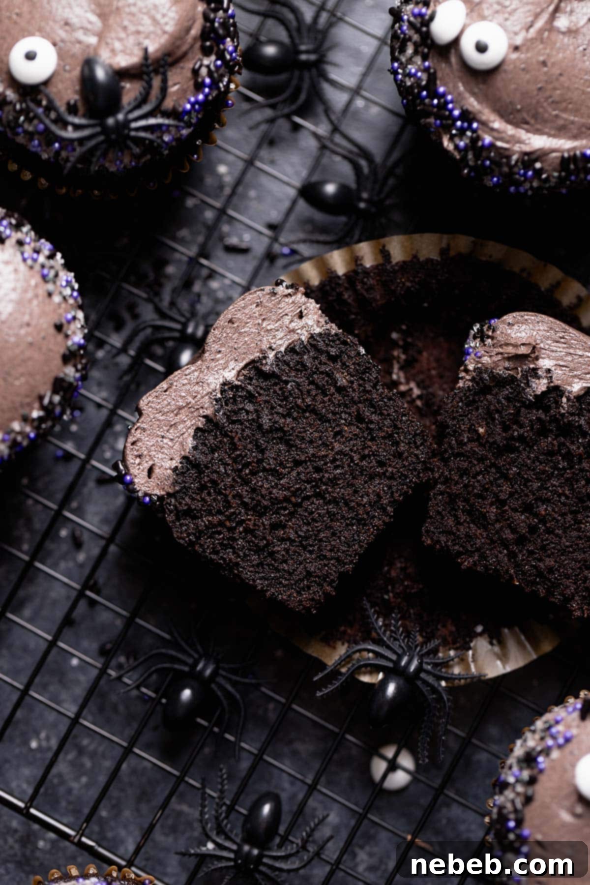 A black chocolate cupcake cut in half on a wire rack, showcasing its incredibly moist interior and fine crumb.