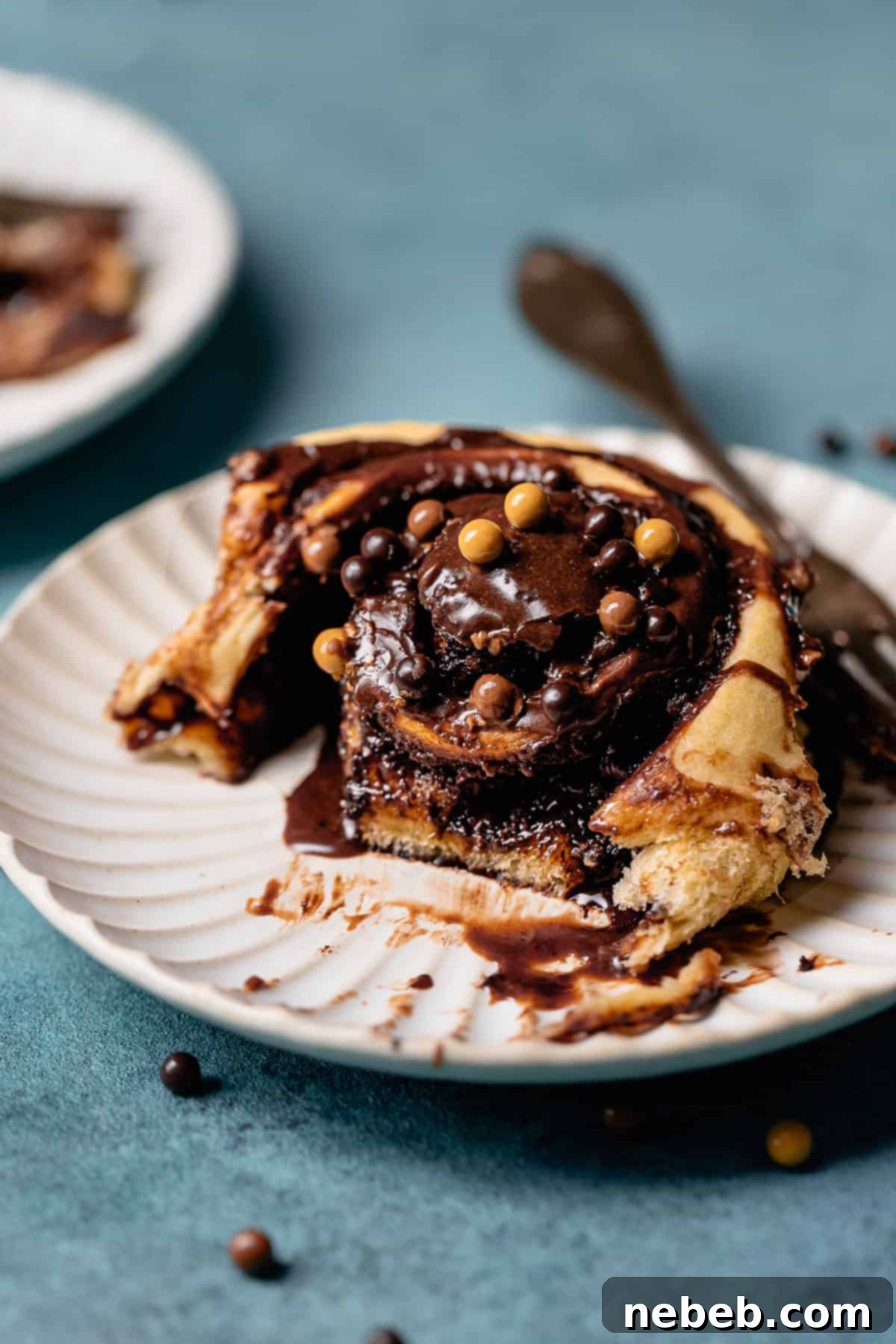 A chocolate bun with a bite taken out of it on a white plate, showcasing the gooey chocolate filling and shiny glaze.