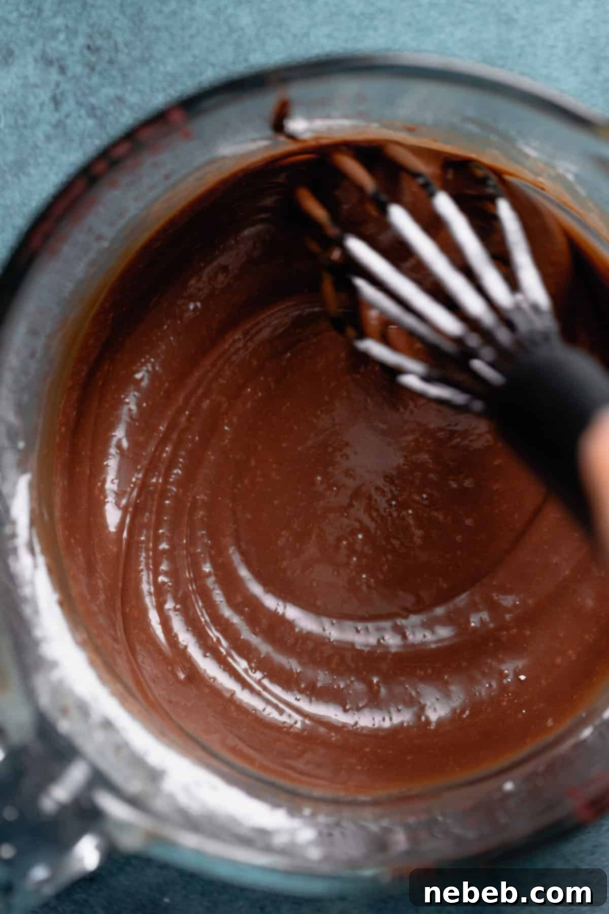 Chocolate icing in a container being whisked to a smooth consistency.