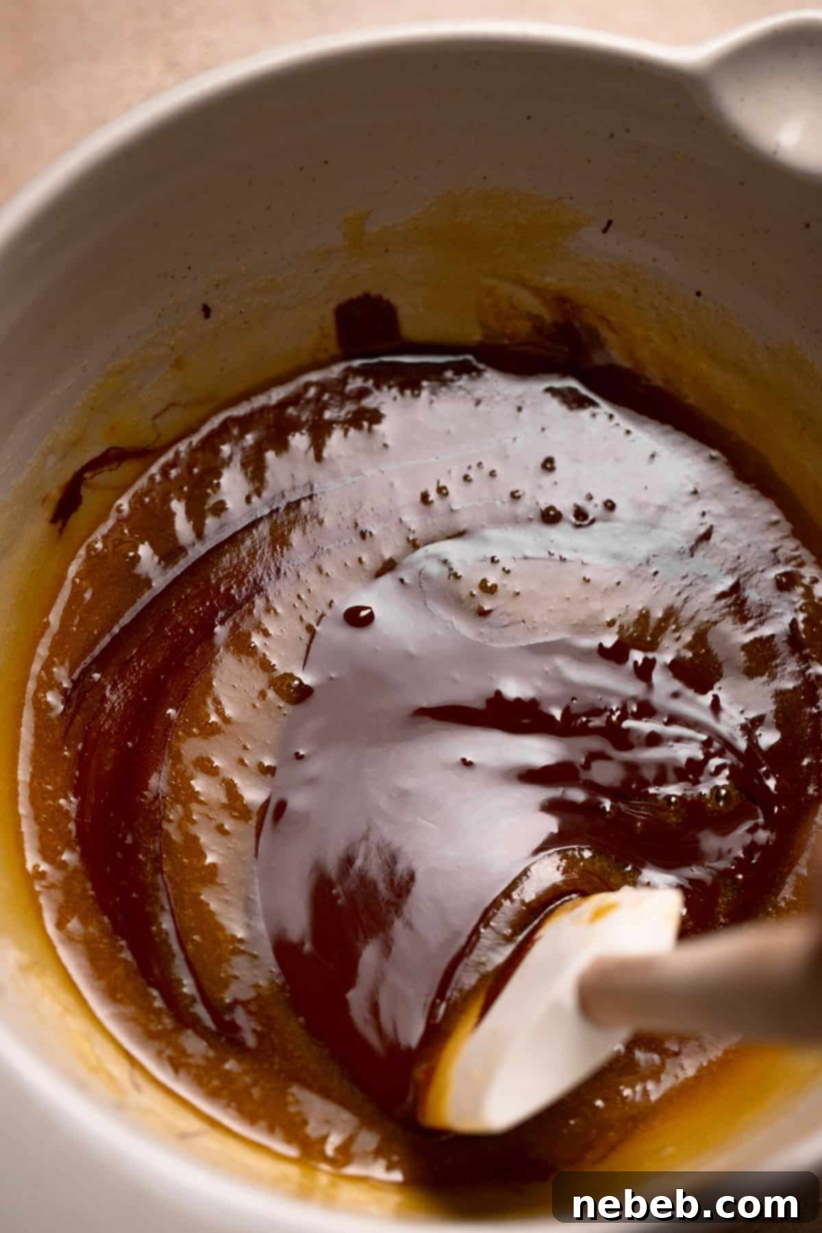 Smooth, glossy melted dark chocolate being carefully incorporated into the sugar, butter, and egg mixture using a flexible spatula.