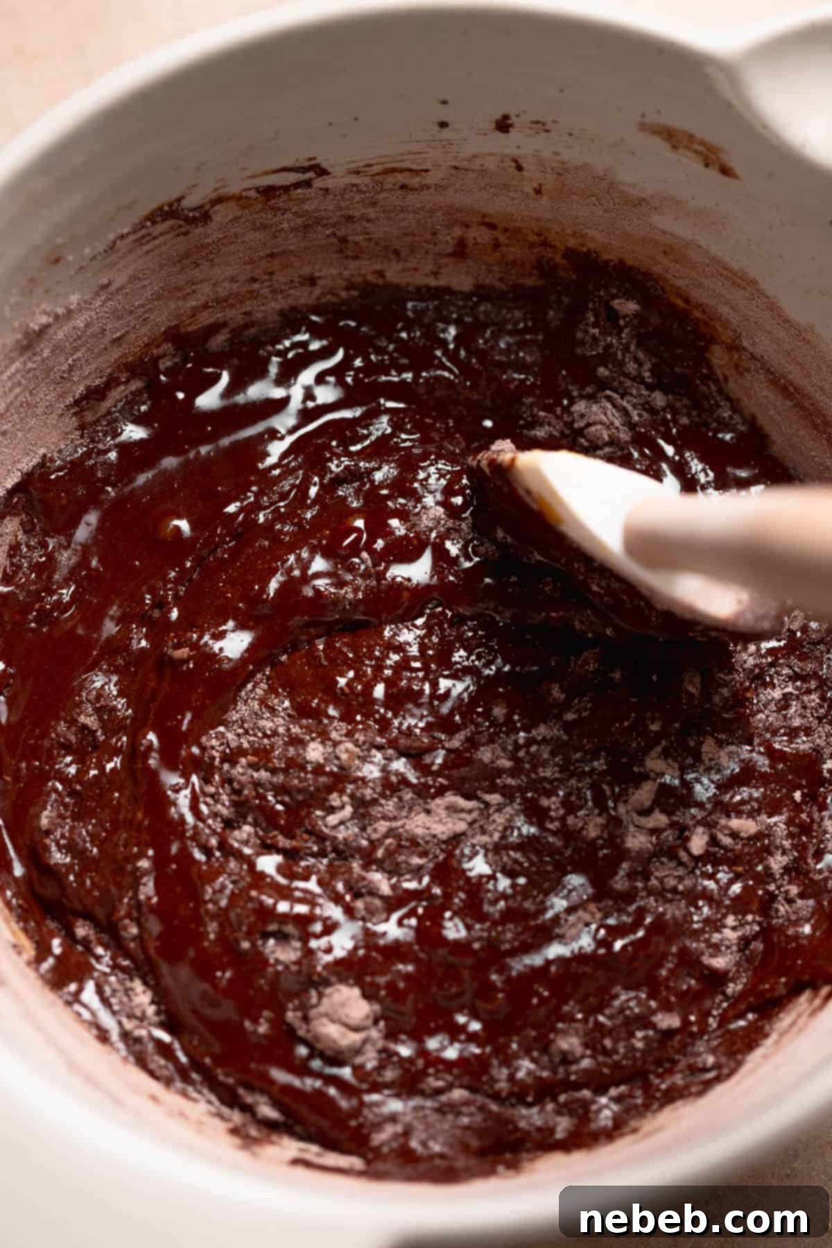 A rubber spatula carefully folding the sifted dry ingredients into the thick, dark chocolate cookie dough, ensuring no streaks remain.