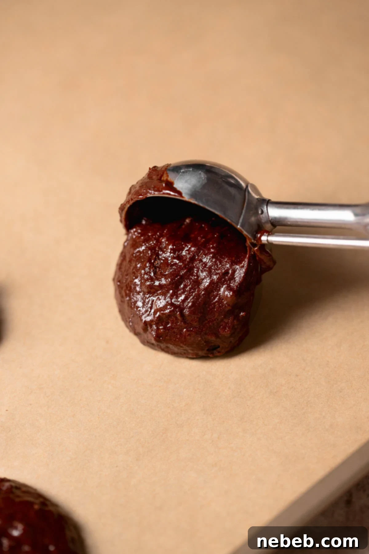 A spring-loaded cookie scoop portioning rich chocolate cookie dough onto a parchment-lined baking tray, preparing for immediate baking.