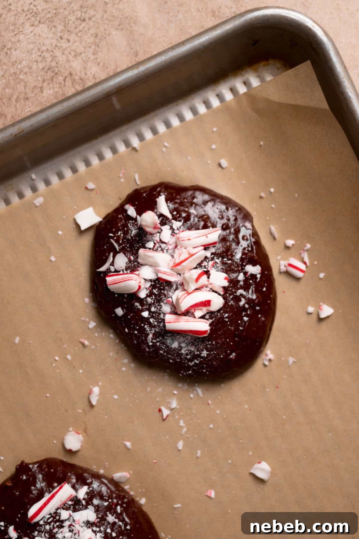 Unbaked chocolate cookie dough scoops, liberally adorned with festive crushed candy cane pieces, arranged on a baking tray before entering the oven.