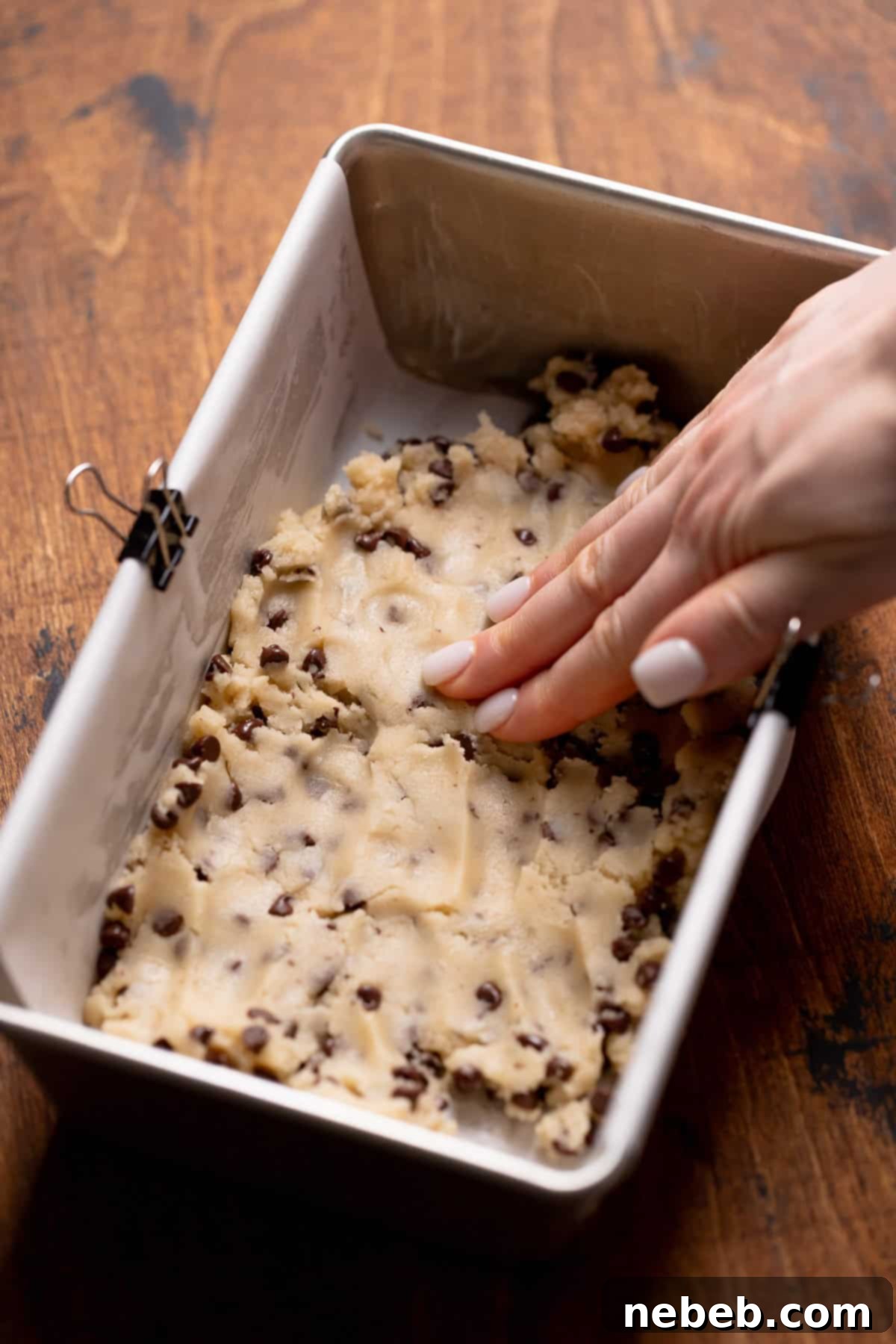 A hand pressing the cookie dough into the loaf pan, preparing for baking.