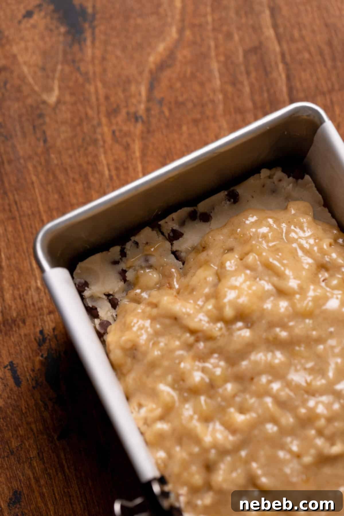 An overhead shot of the banana bread batter covering the cookie dough layer in a loaf pan.