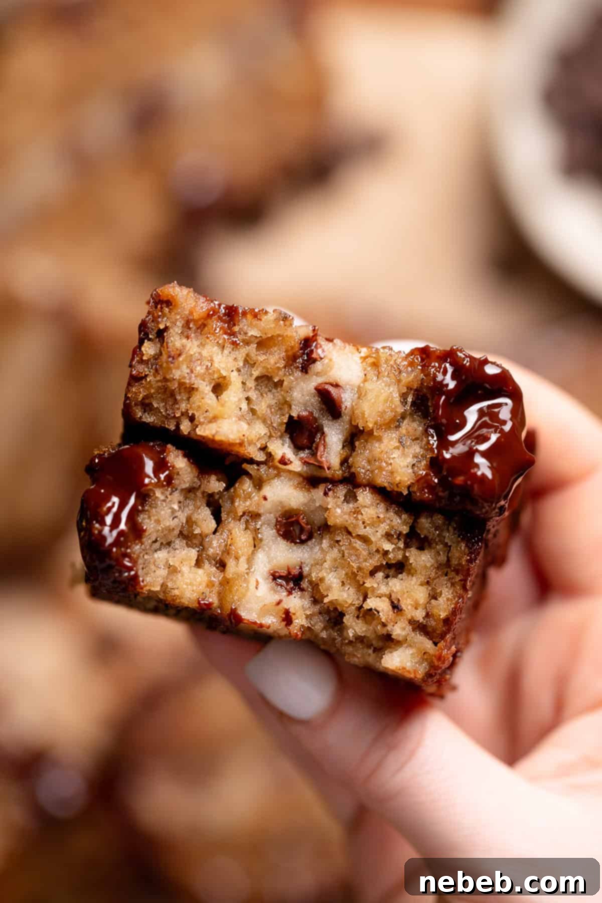 A hand holding a piece of cookie dough banana bread, showcasing the distinct, gooey chocolate chip cookie dough center.
