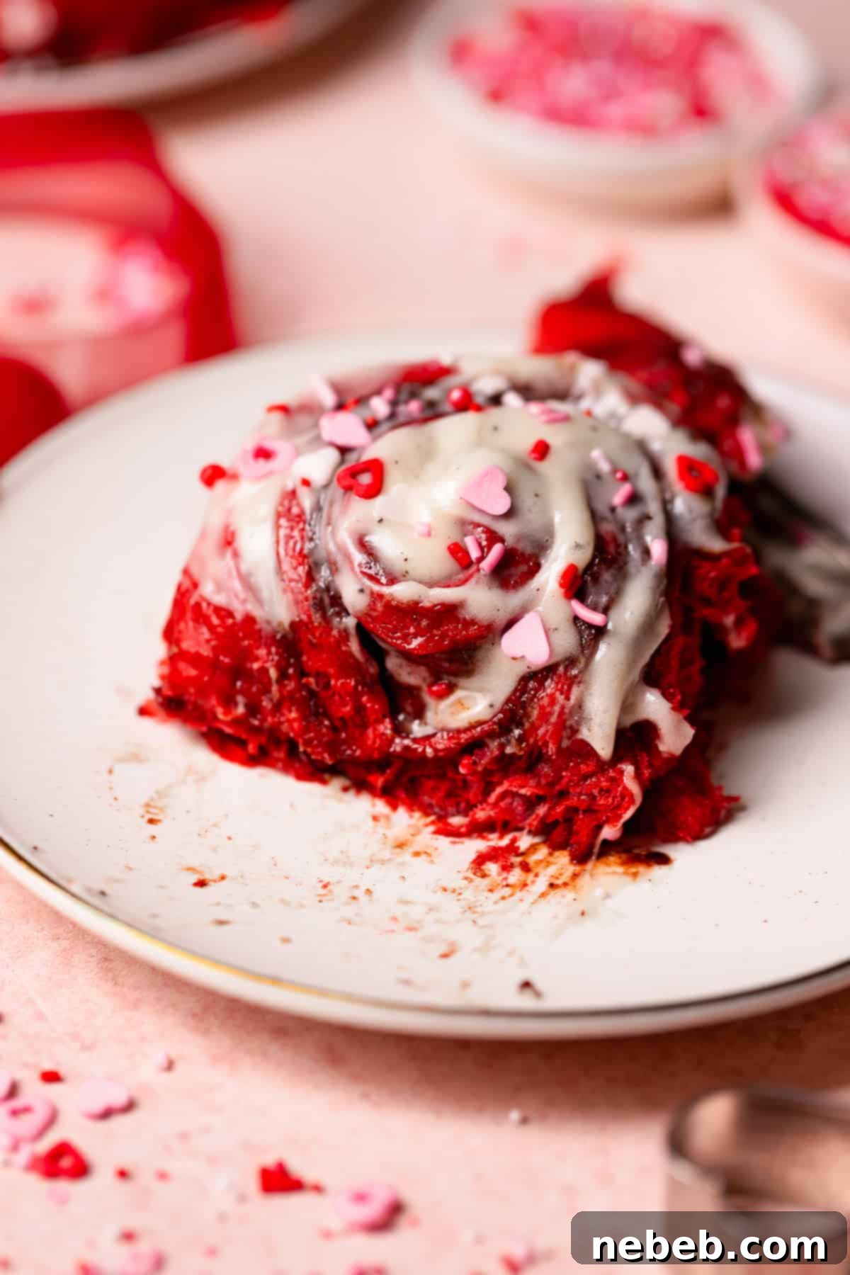 A red velvet roll on a white plate with pink heart sprinkles.