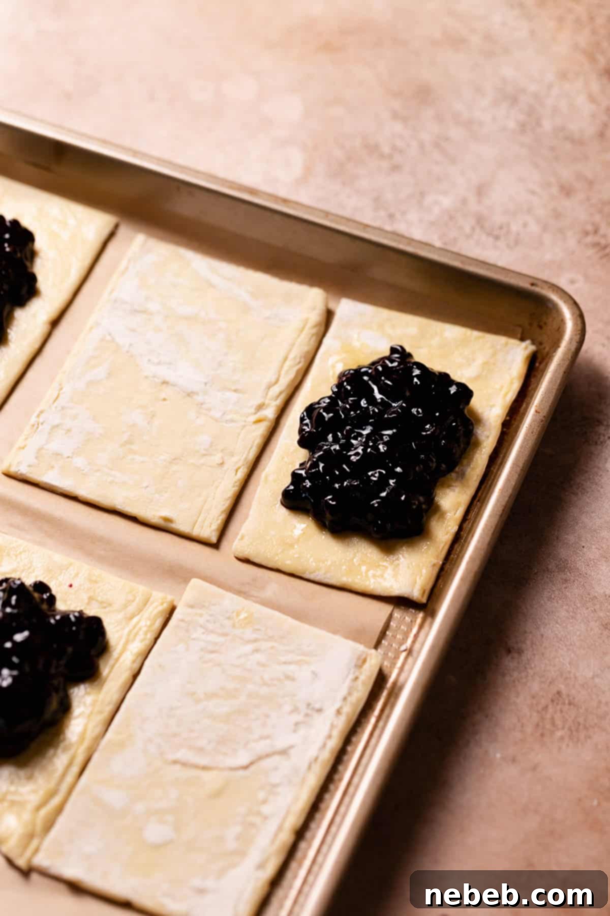 Squares of puff pastry on a baking sheet, with half filled with luscious blueberry jam.