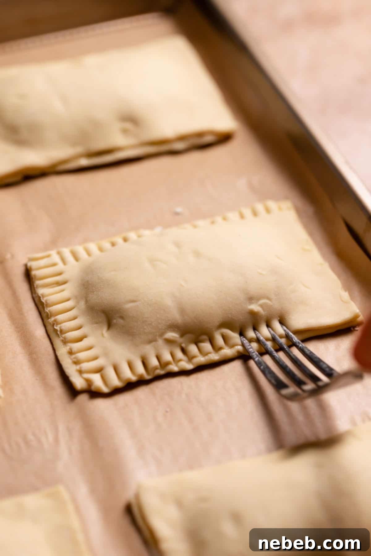 A fork crimping the edges of the filled toaster pastries, sealing in the blueberry jam.