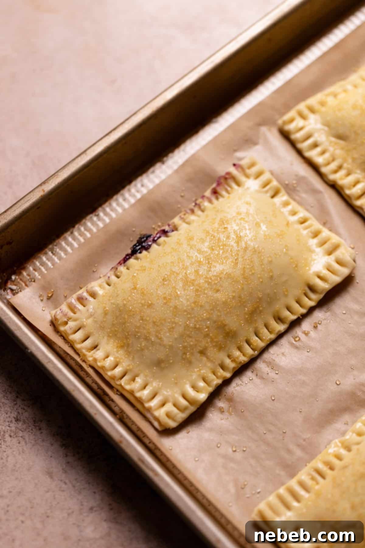 Filled toaster pastries on a baking sheet covered in turbinado sugar, ready for baking.
