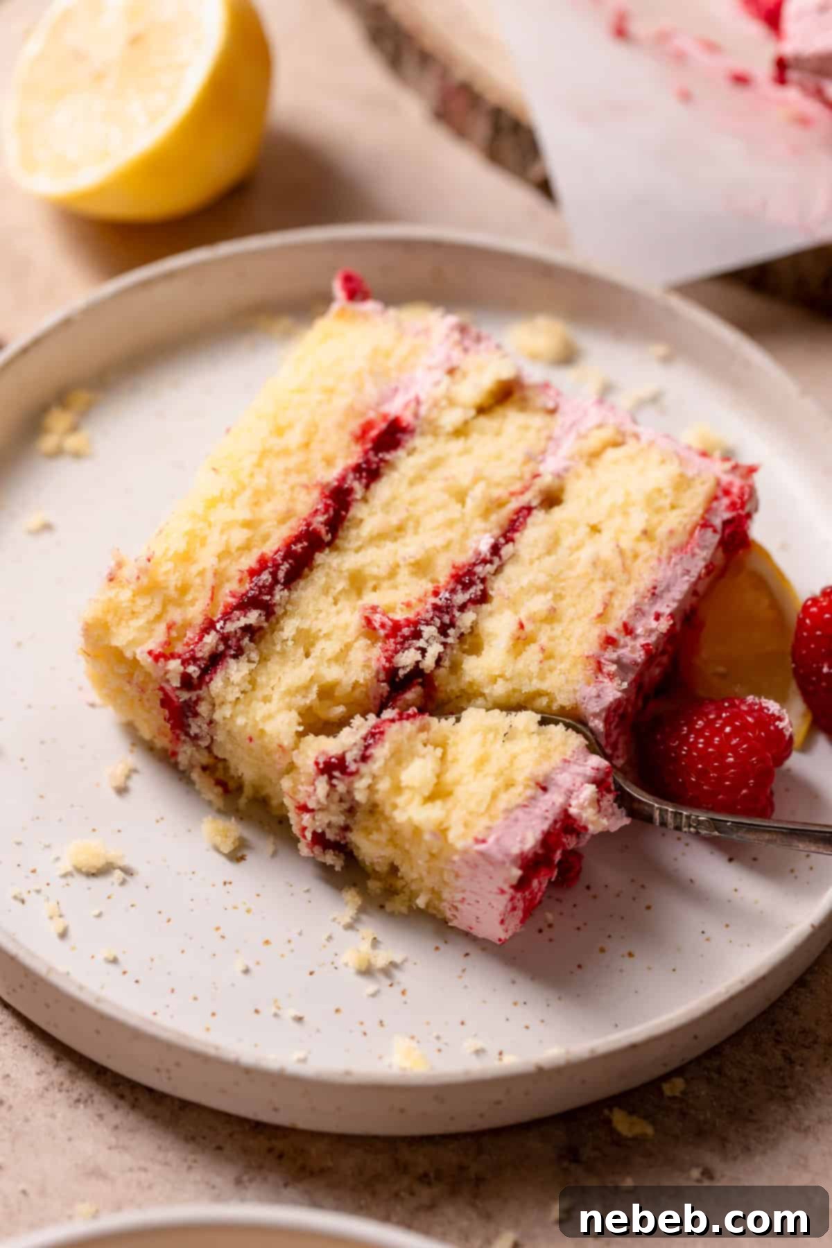 Zesty Lemon Raspberry Delight 13 A close-up of a slice of the raspberry lemon cake on a white speckled plate, with a fork poised to take a bite, highlighting its moist interior and fruit filling.