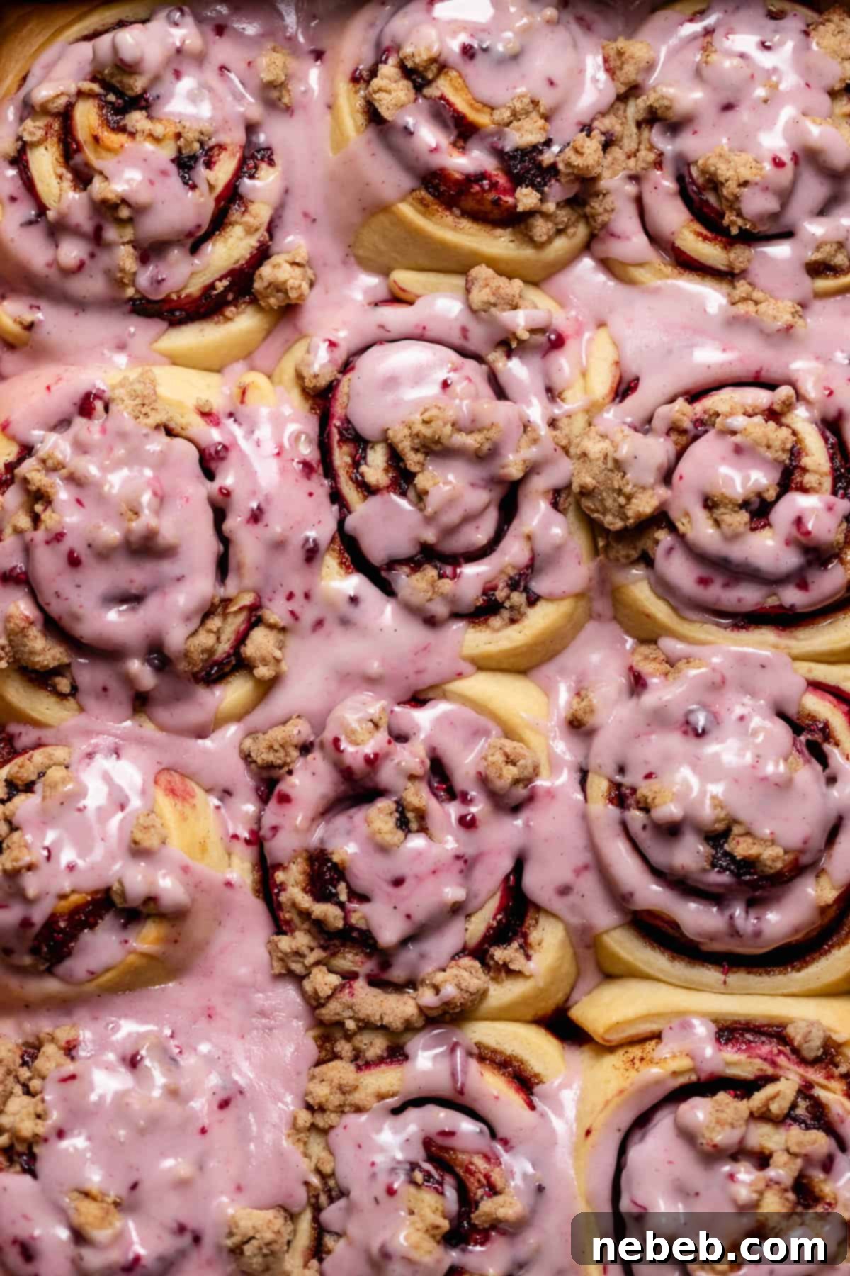 Freshly baked blackberry raspberry cinnamon rolls with a generous layer of berry frosting and crumb topping, glistening in a baking pan.