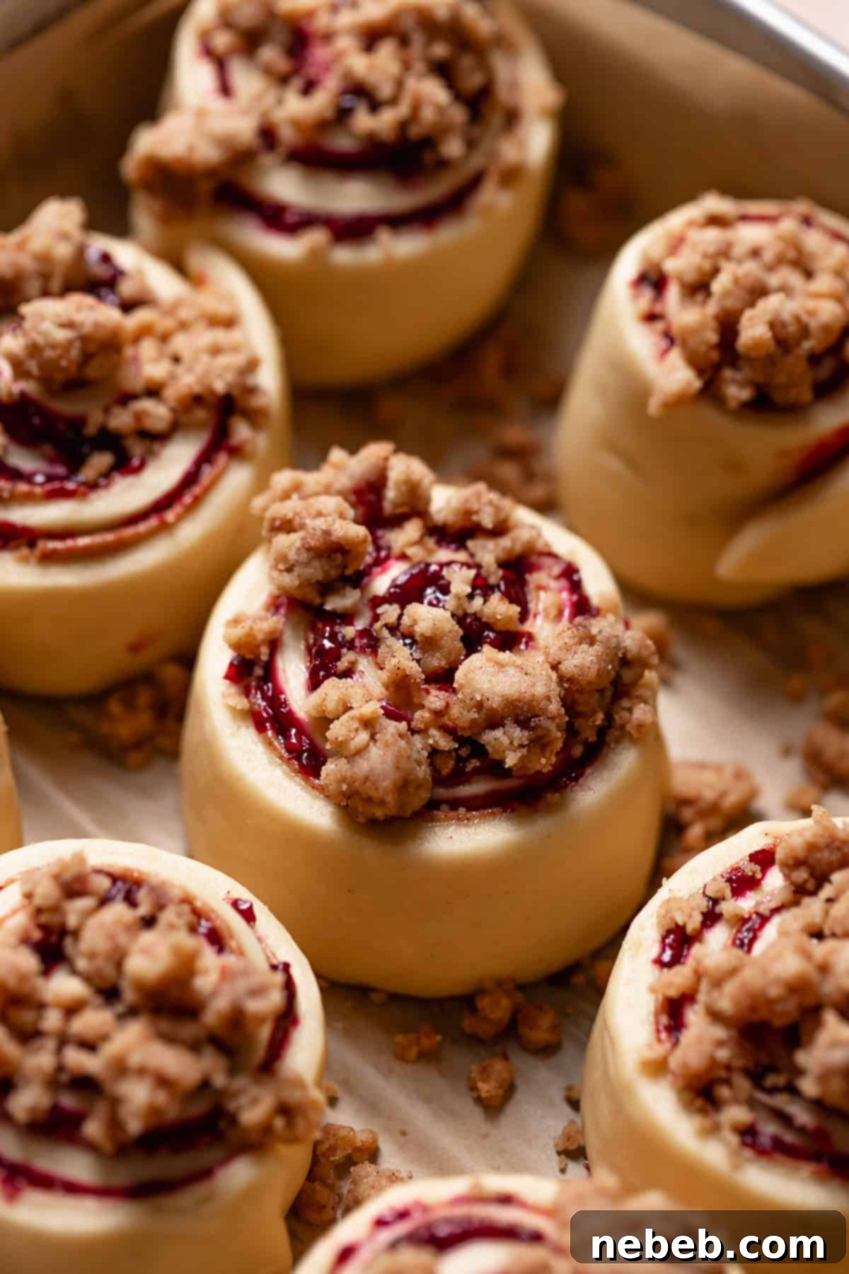 A cinnamon roll generously topped with a buttery crumb mixture, ready for baking.