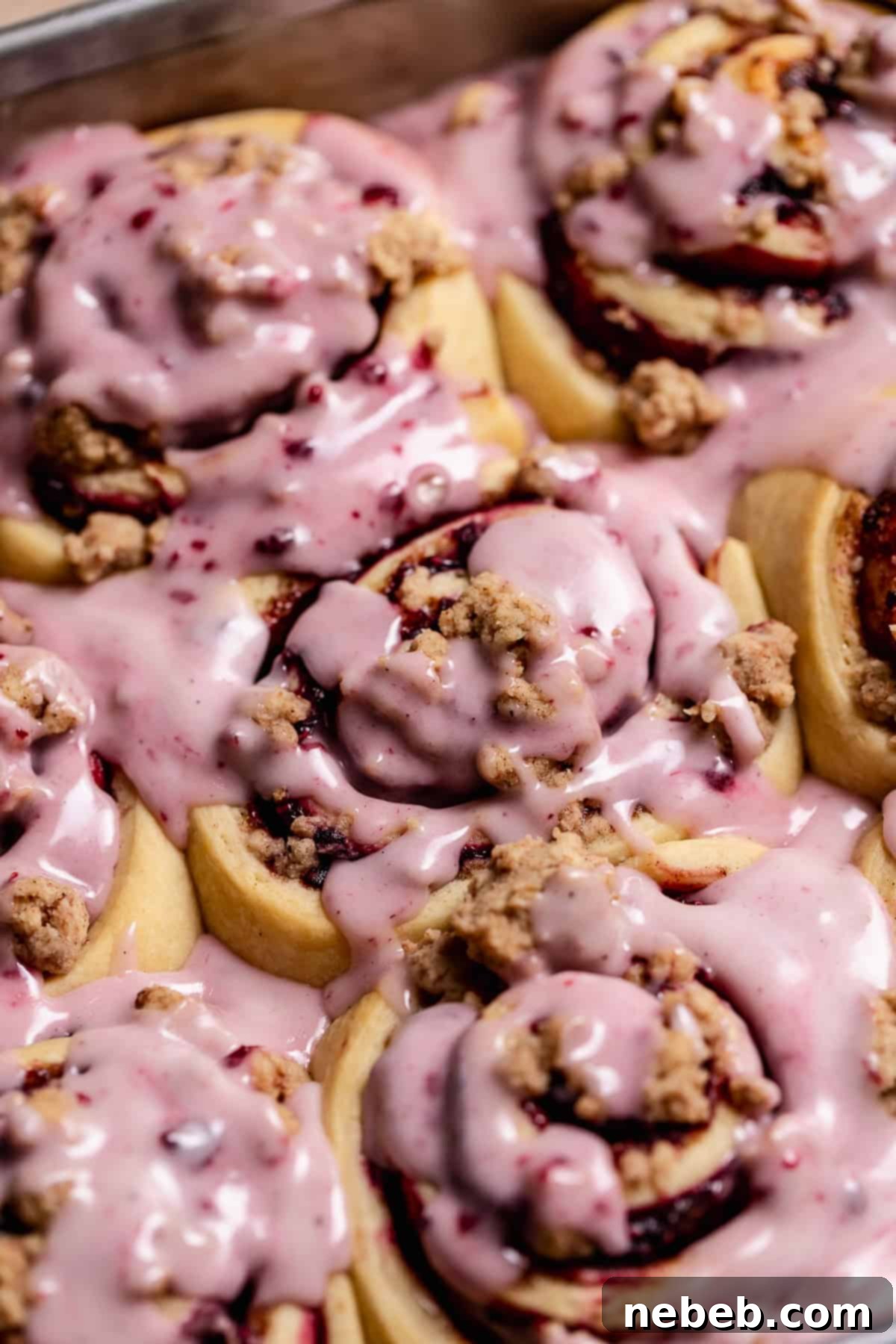 A side view of the baked blackberry raspberry cinnamon rolls, covered with a sweet berry glaze.