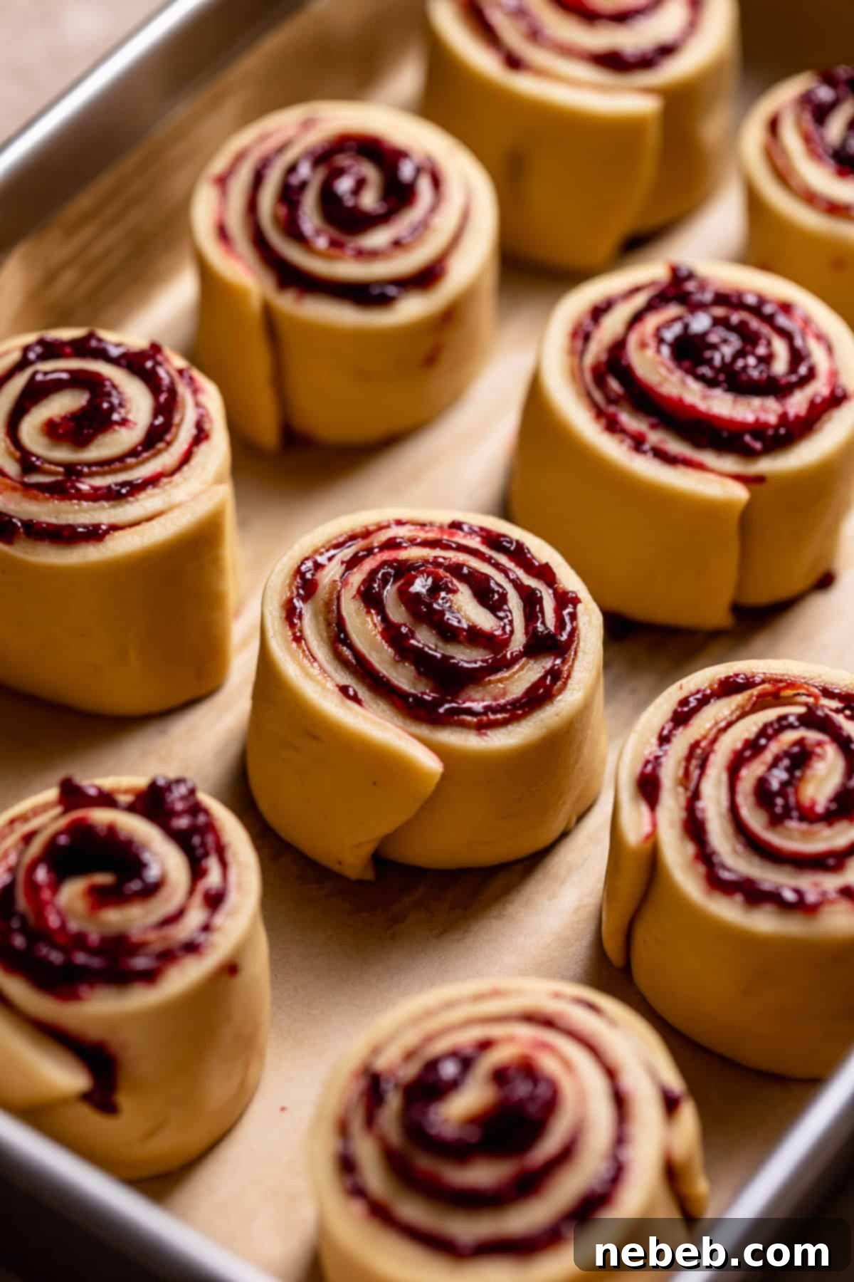 Berry-swirled cinnamon rolls neatly arranged in a baking pan, prior to their second rise.