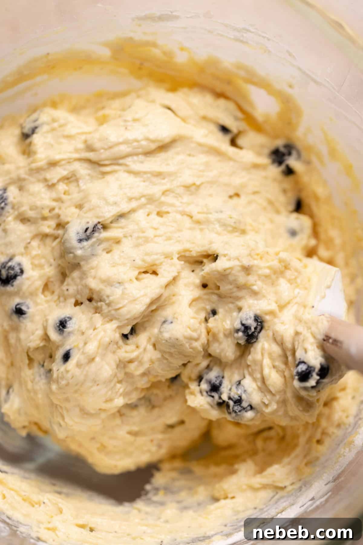 A spatula folding the fresh blueberries into the cake batter.