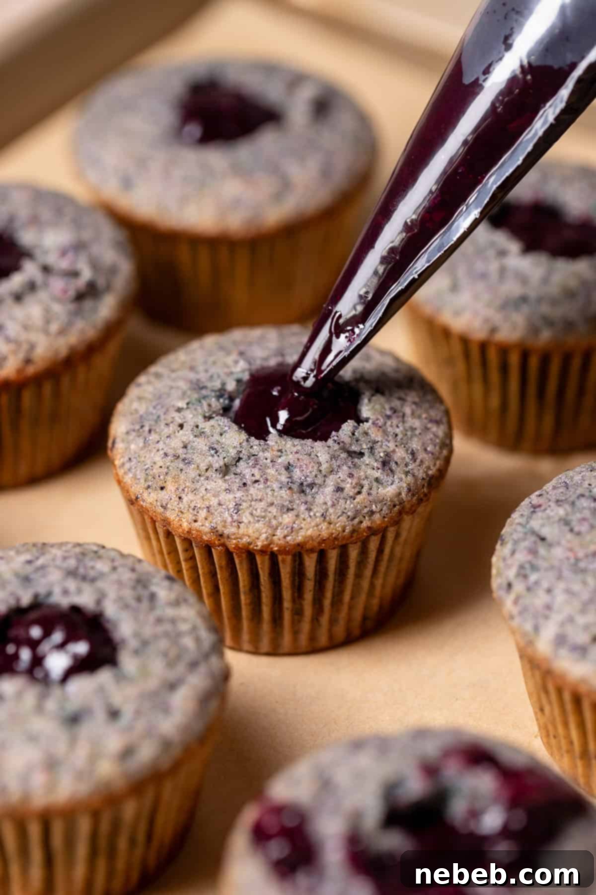 A piping bag filling the center of a cupcake with blueberry filling.
