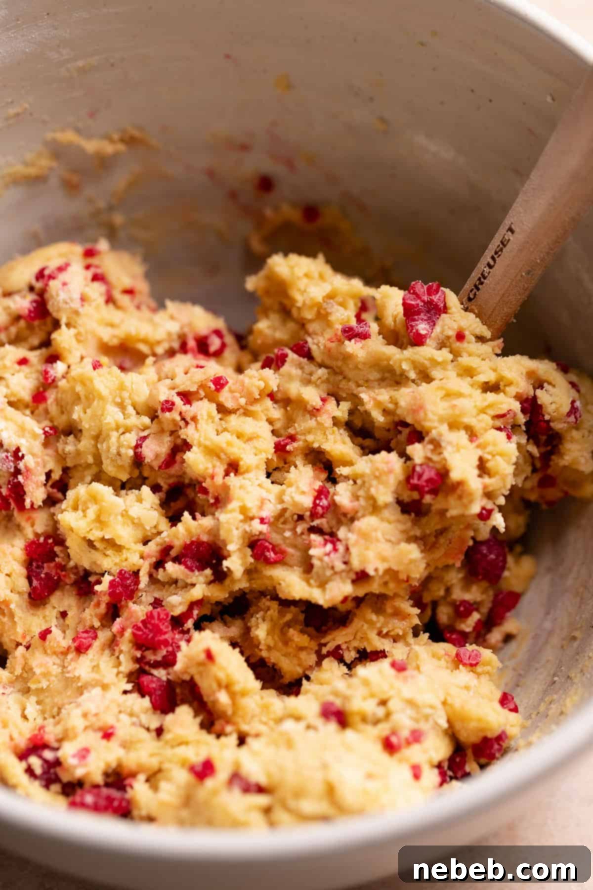 Lemon cookie dough with frozen raspberry bits being folded in.