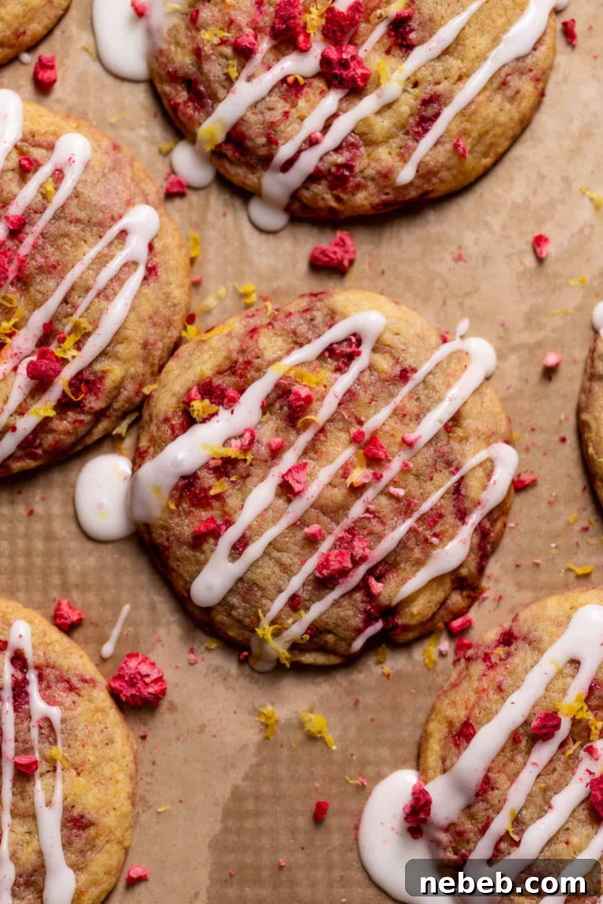 Cookies on a baking sheet drizzled with lemon glaze and sprinkled with raspberries and lemon zest.