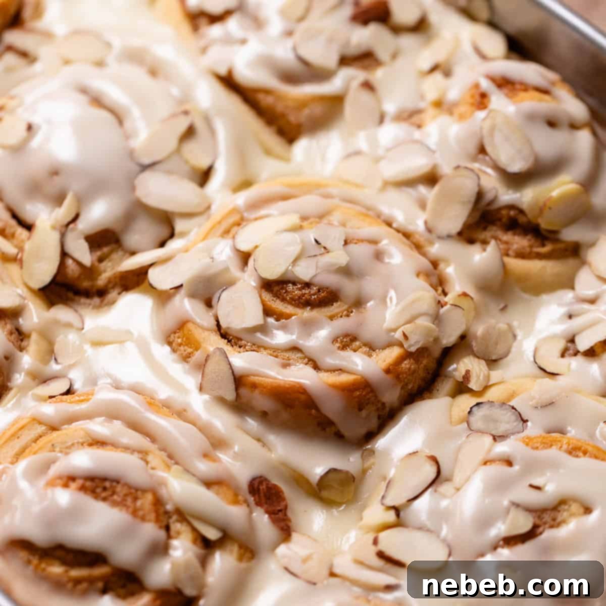 Almond croissant rolls in a baking pan with almond glaze and sliced almonds.