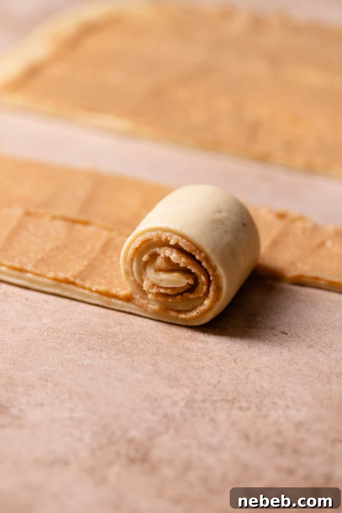 A strip of cinnamon roll dough being rolled up into a bun.