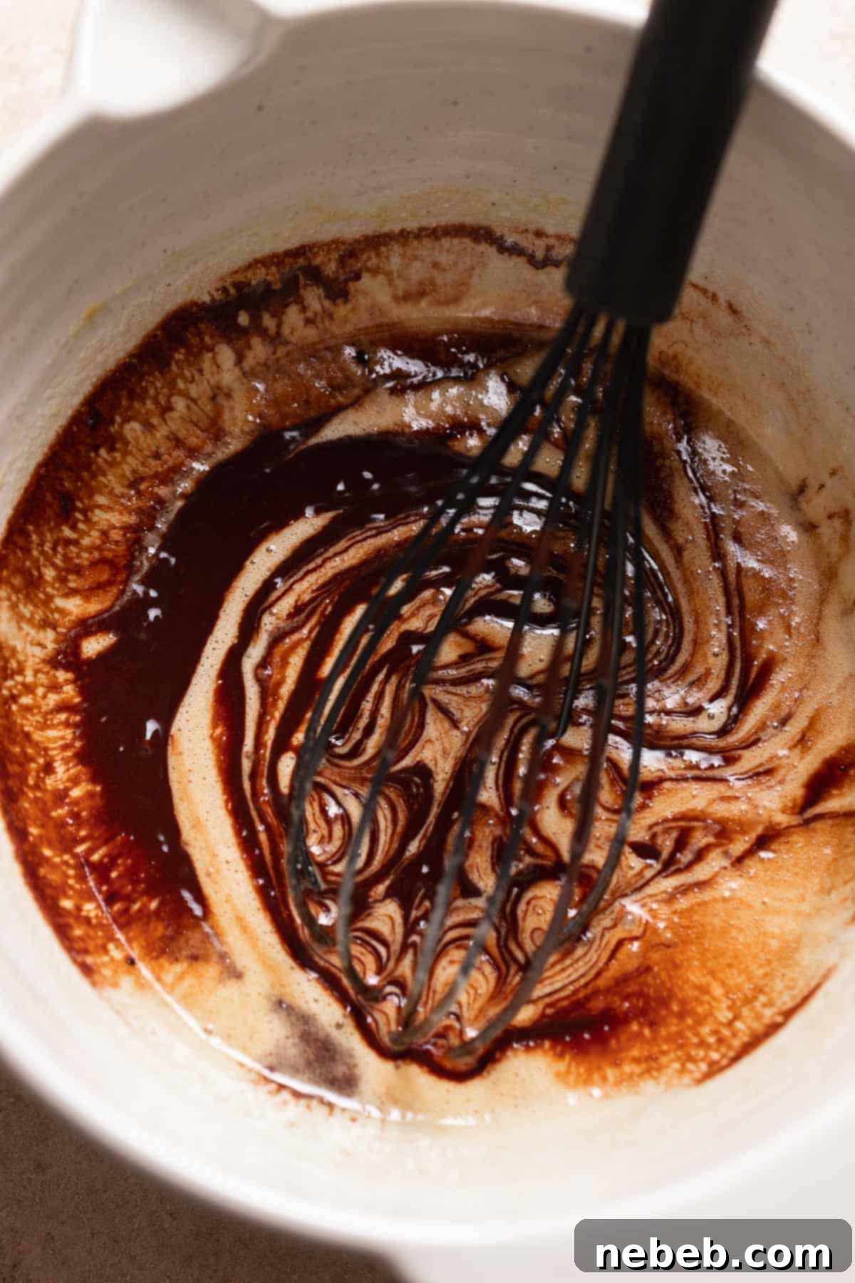 A mixing bowl with a whisk blending melted chocolate into whipped eggs and sugar for fudgy brownies.